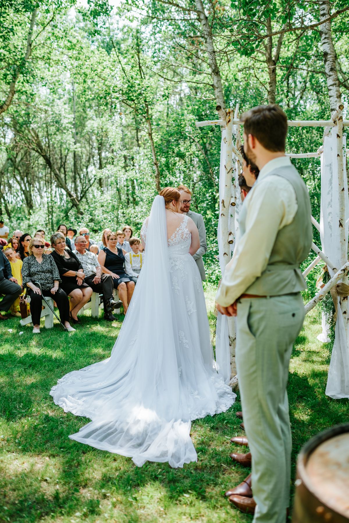 Couple at the ceremony under the handmade log arbor in the birch forest at Deer Meadow Farm Manitoba
