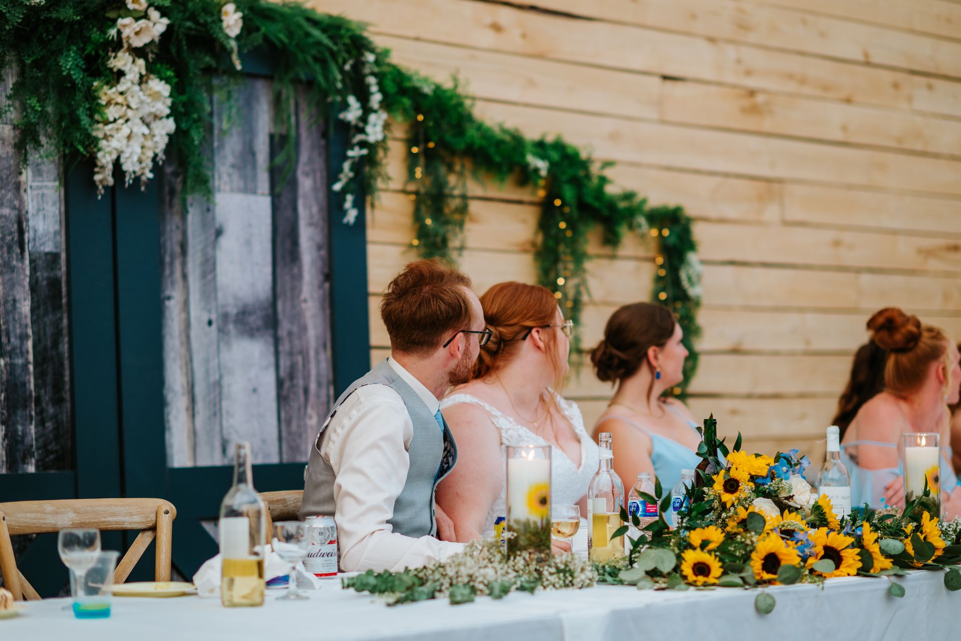 Alysia and Josh at the head table with sunflower garland at Deer Meadow Farm Manitoba reception