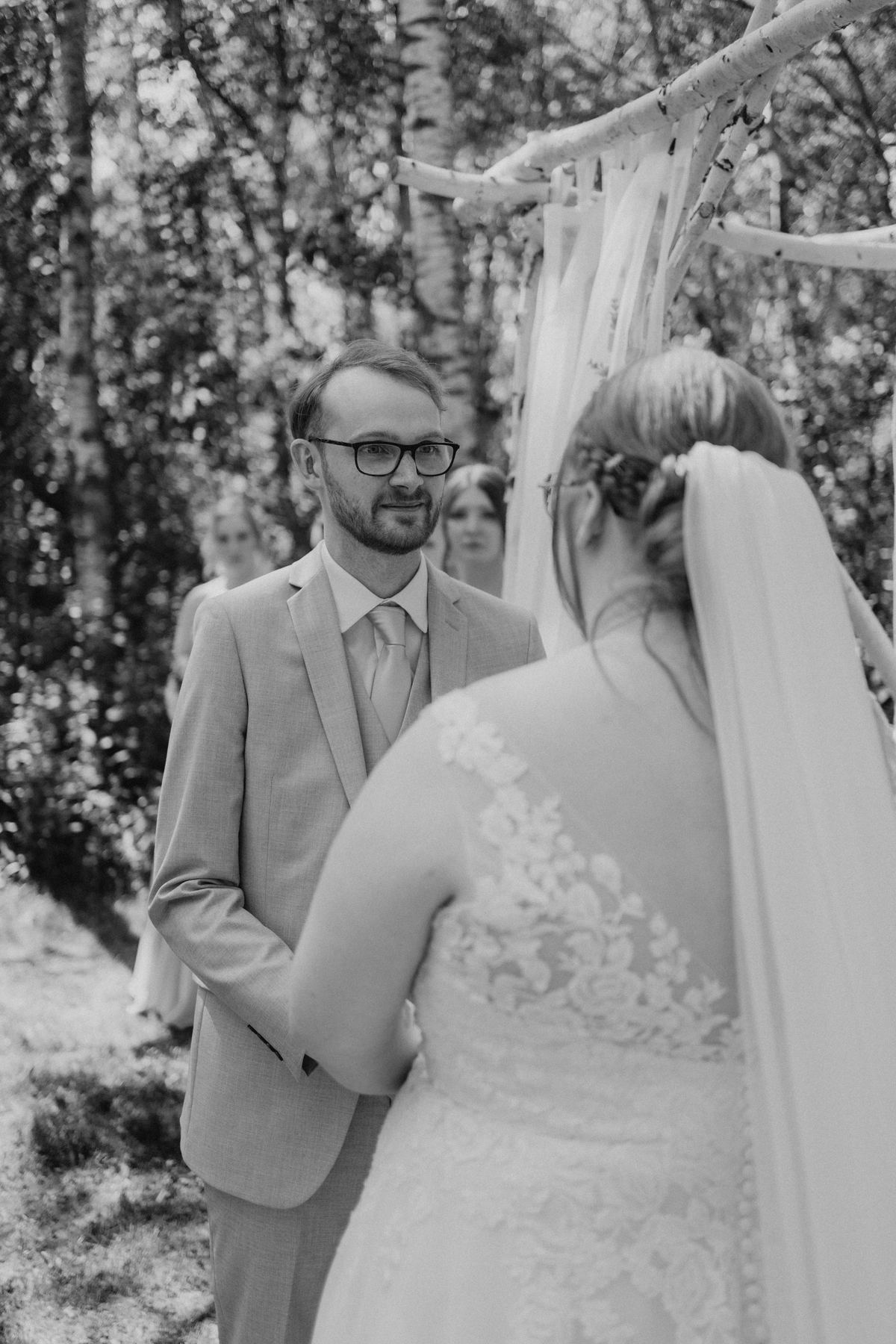 Couple exchanging vows under the log arbor at Deer Meadow Farm Manitoba — wedding photography by Ngo Photography
