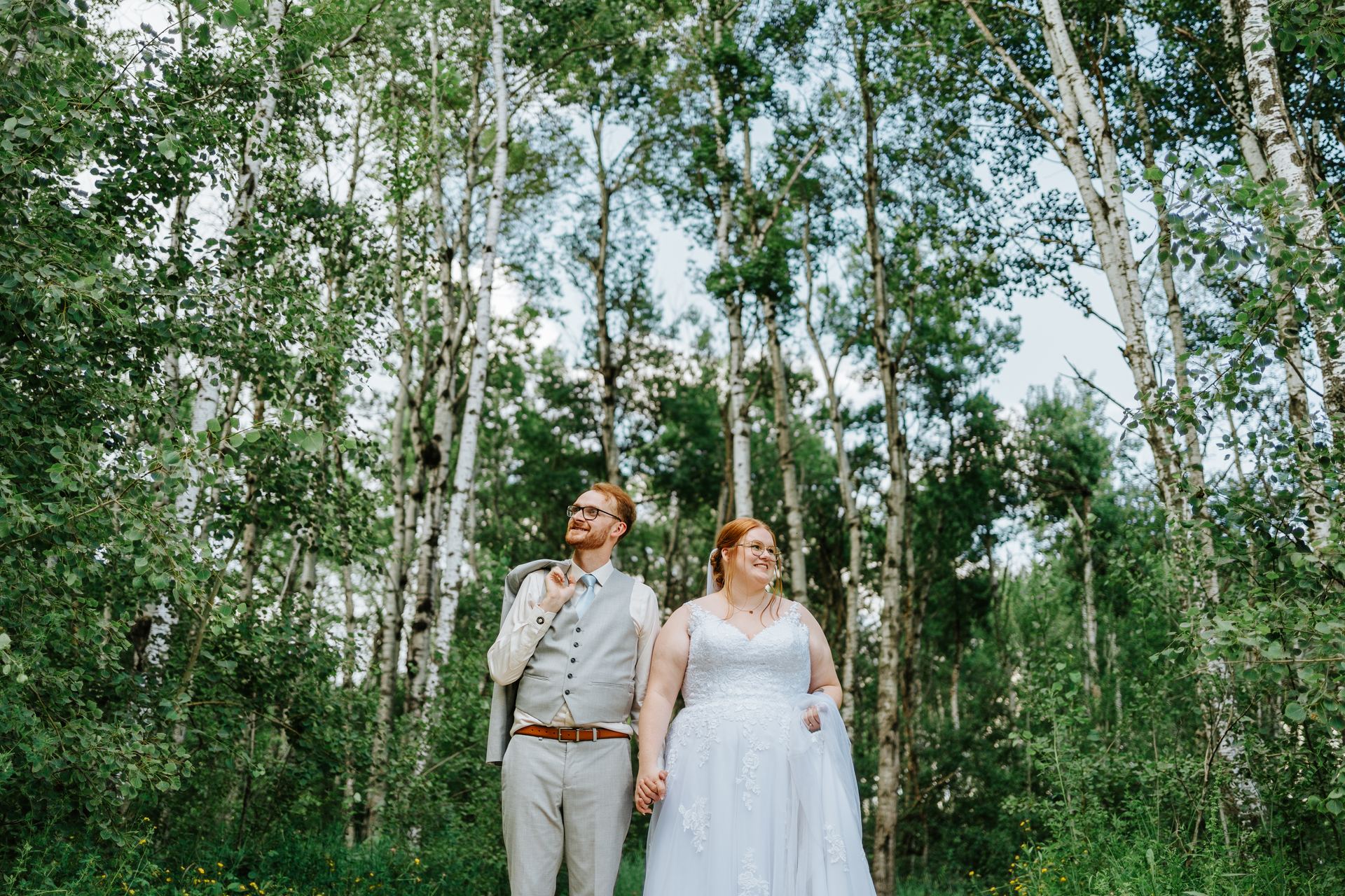 Alysia and Josh walking hand in hand through the sunlit birch forest at Deer Meadow Farm Manitoba — Ngo Photography