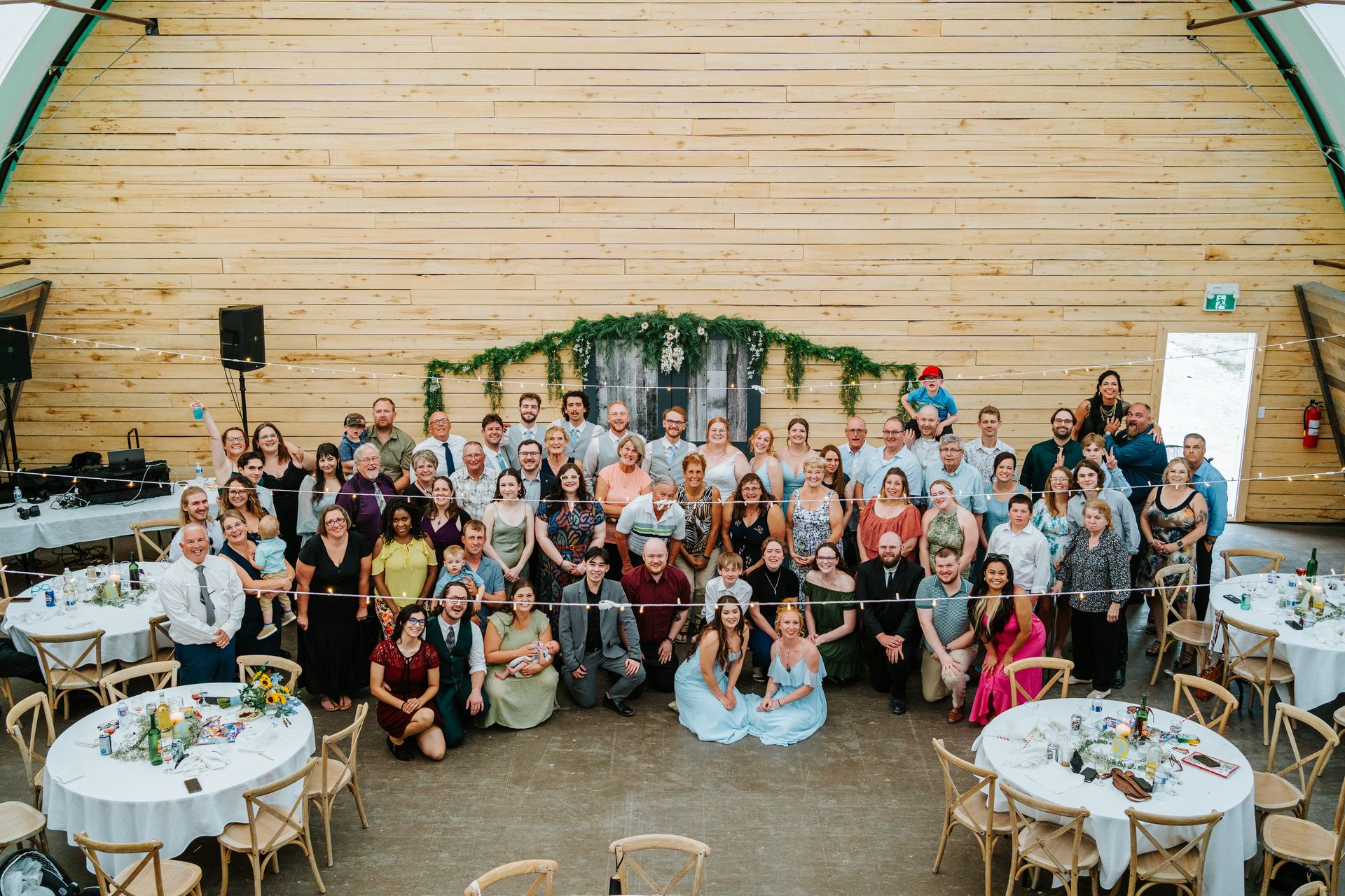 Full wedding guest group photo taken from the mezzanine of the quonset barn at Deer Meadow Farm Manitoba