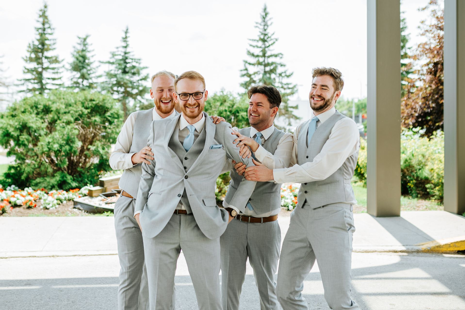 Groom Josh and groomsmen in matching light grey suits laughing together — Deer Meadow Farm wedding Manitoba