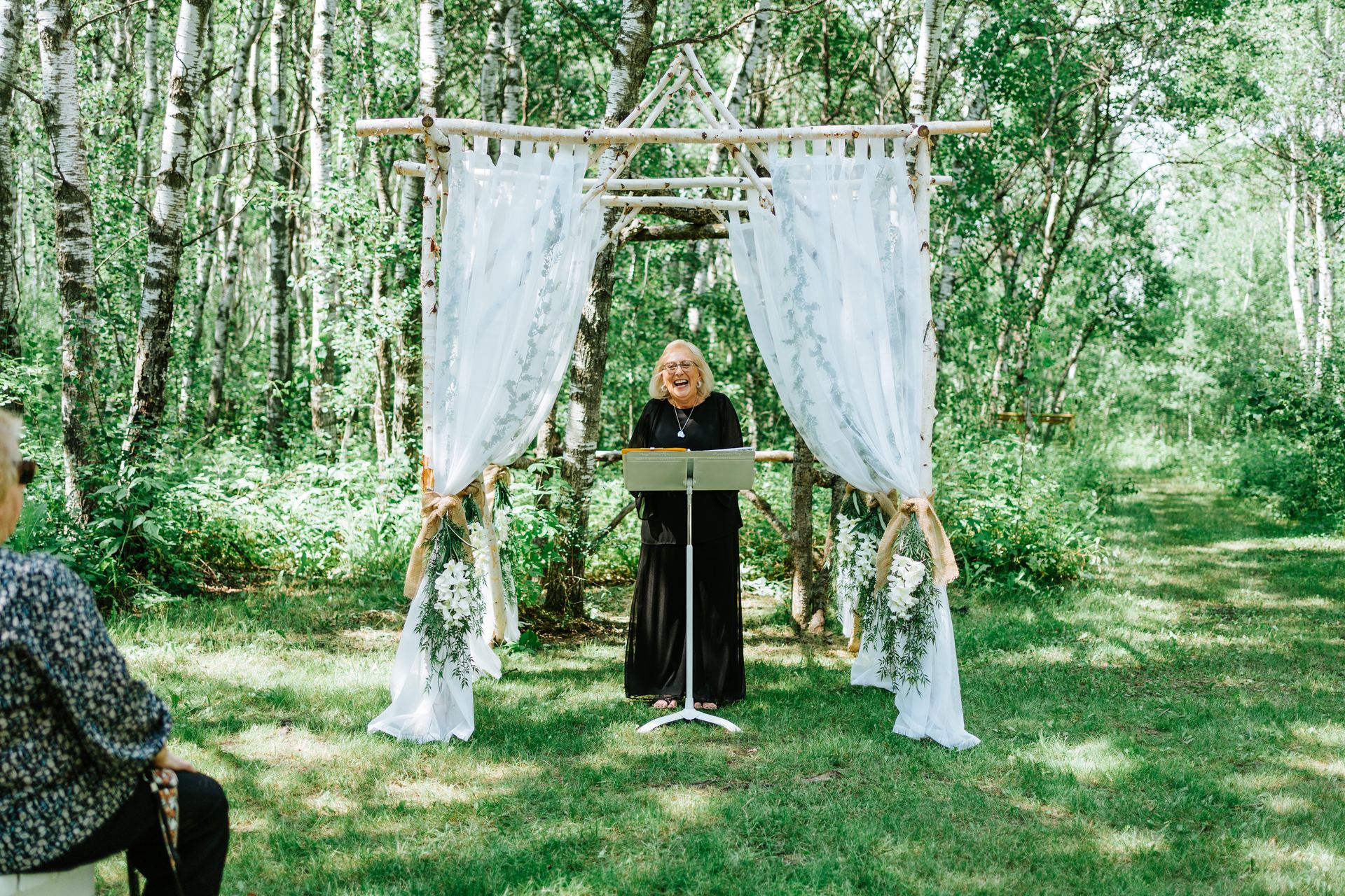 Officiant at the handmade birch log arbor in the ceremony at Deer Meadow Farm Manitoba wedding