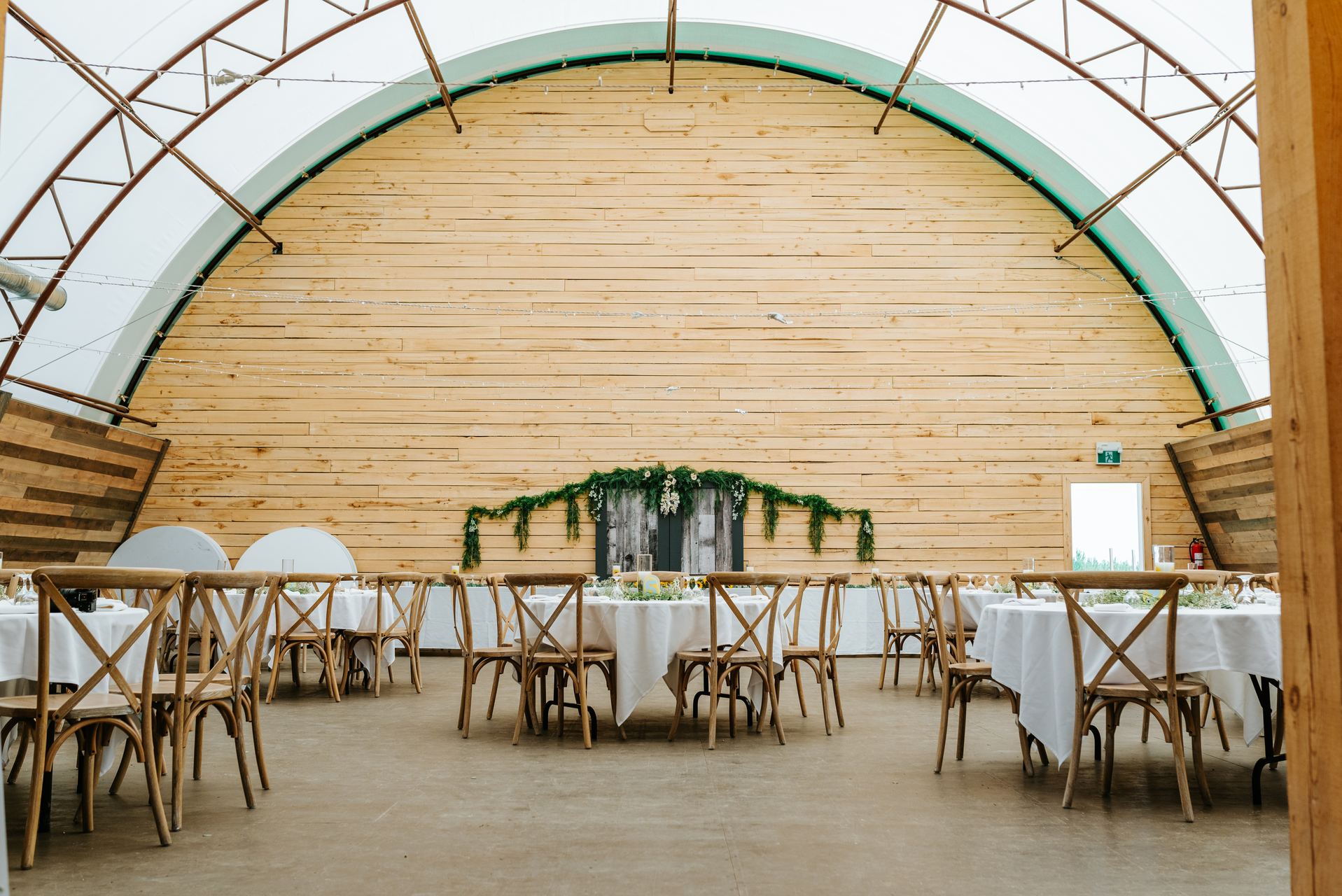 Quonset barn reception hall setup at Deer Meadow Farm Manitoba — arching wooden ceiling and cross-back chairs