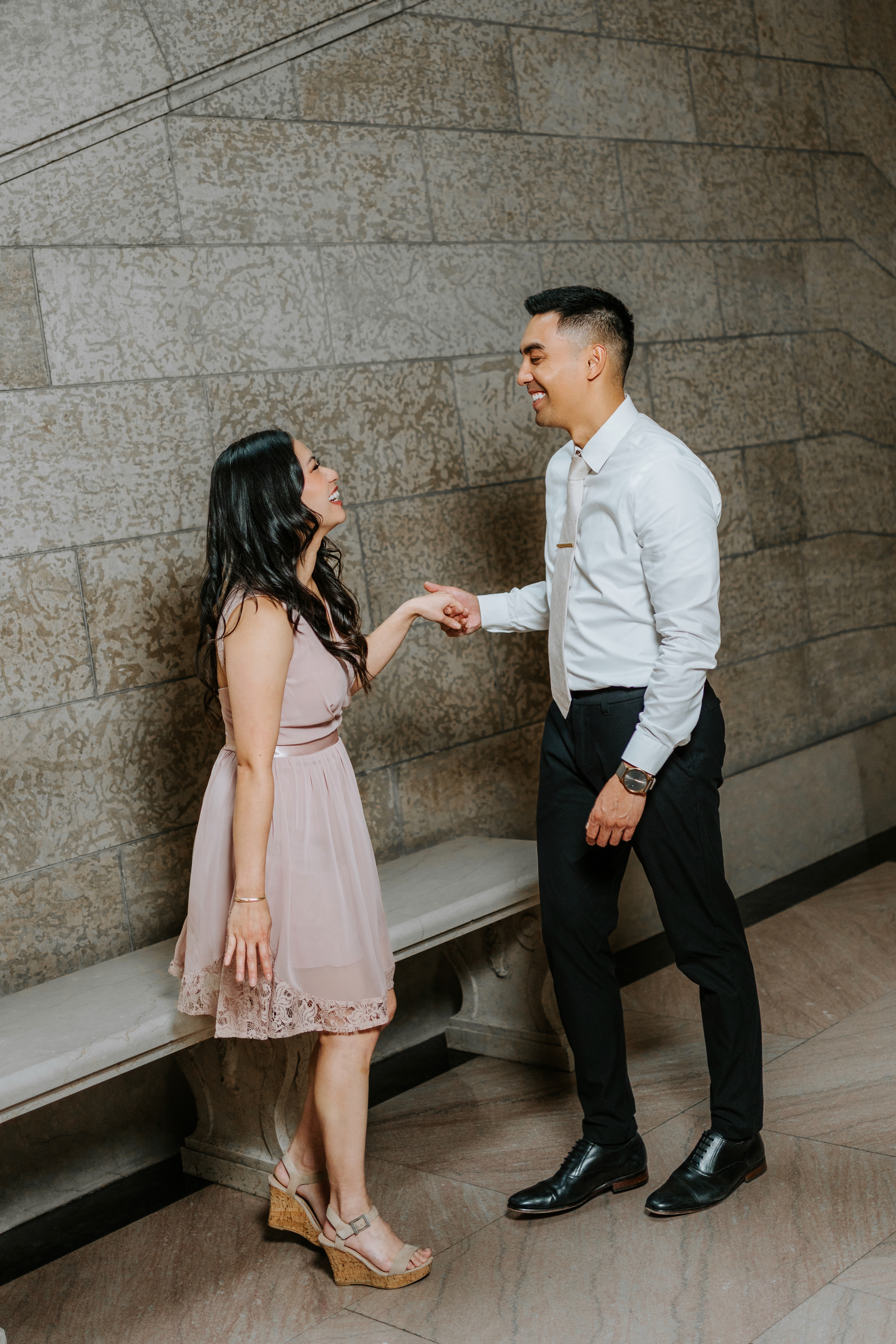 AJ and Julie laughing together against the warm limestone wall of the Manitoba Legislative Building — engagement photography by Ngo Photography