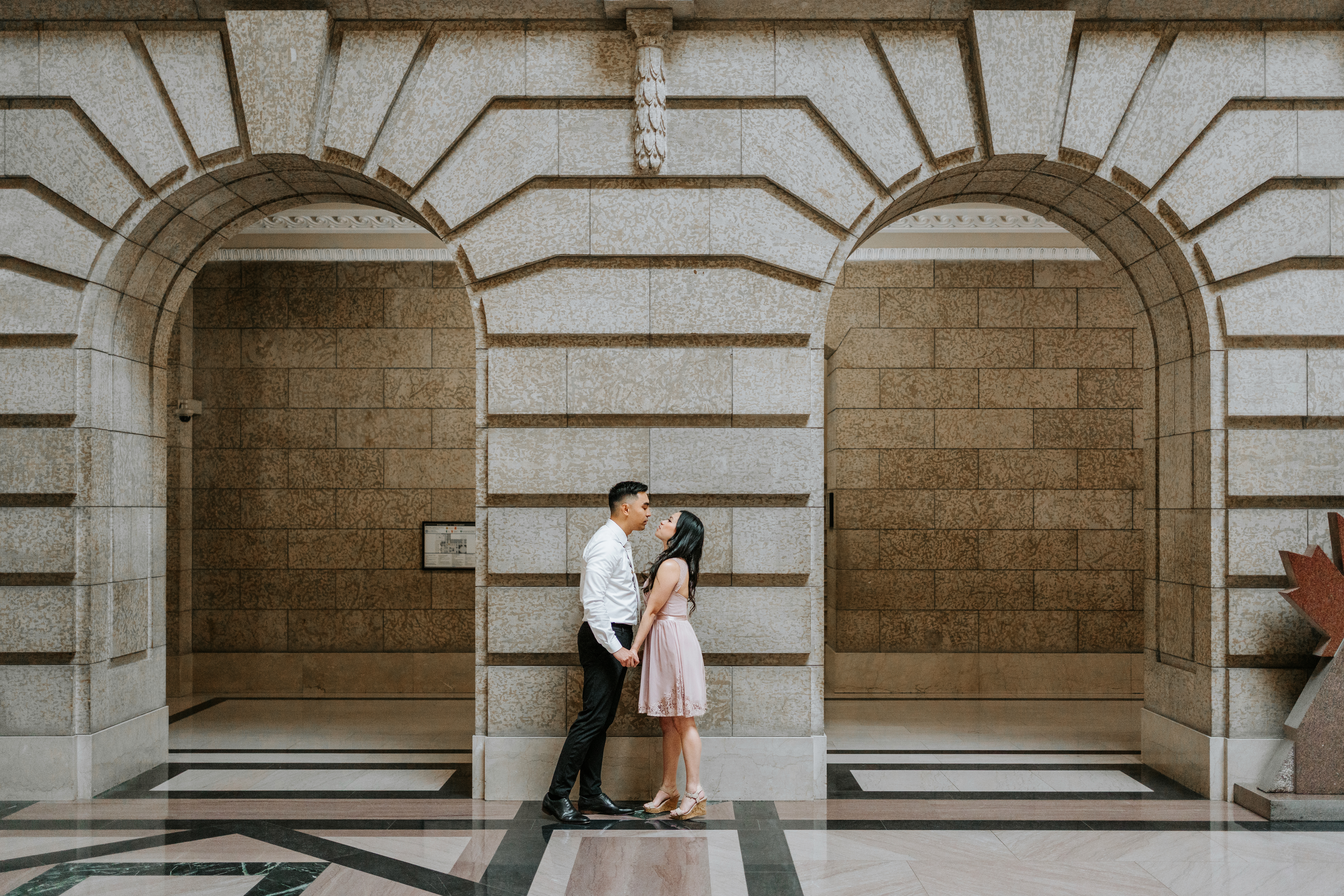 AJ and Julie facing each other about to kiss framed by twin stone arches at the Manitoba Legislative Building Winnipeg — Ngo Photography engagement session