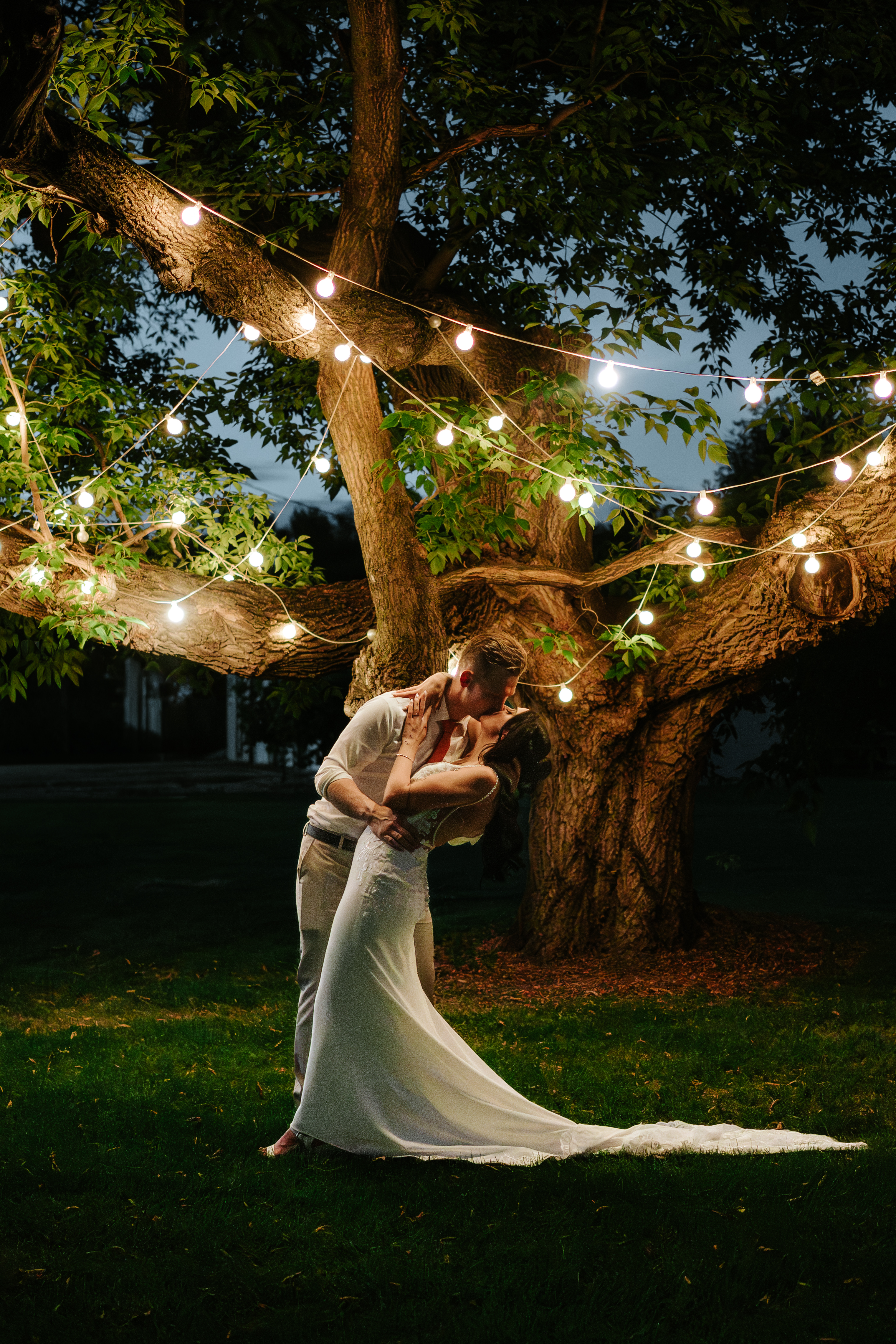 Brandon and Selena dipping under string lights in a tree at night at Ashgrove Acres Manitoba — wedding photography by Chris Ngo Ngo Photography