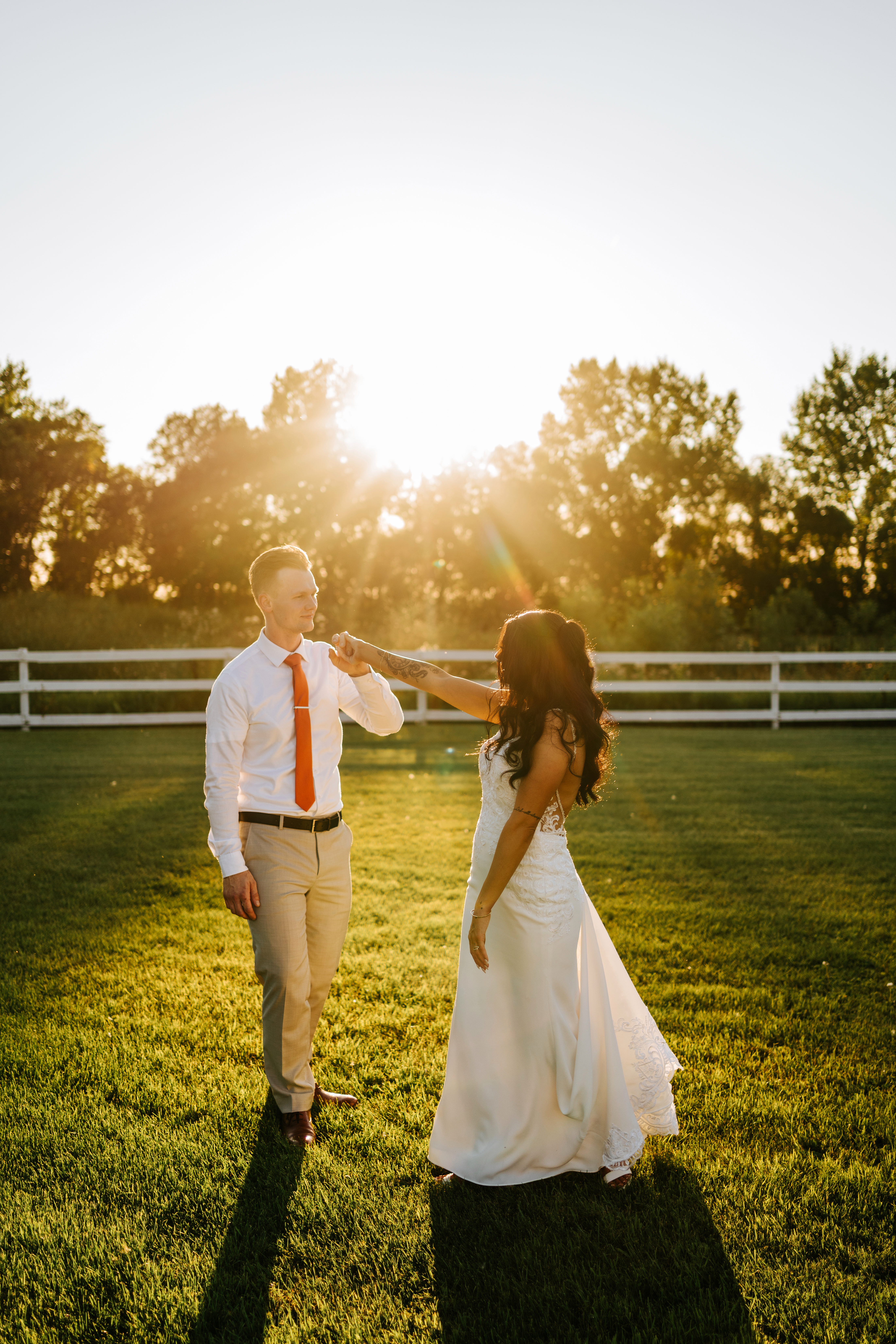Brandon and Selena walking at sunset along white fence at Ashgrove Acres — countryside wedding photography Manitoba