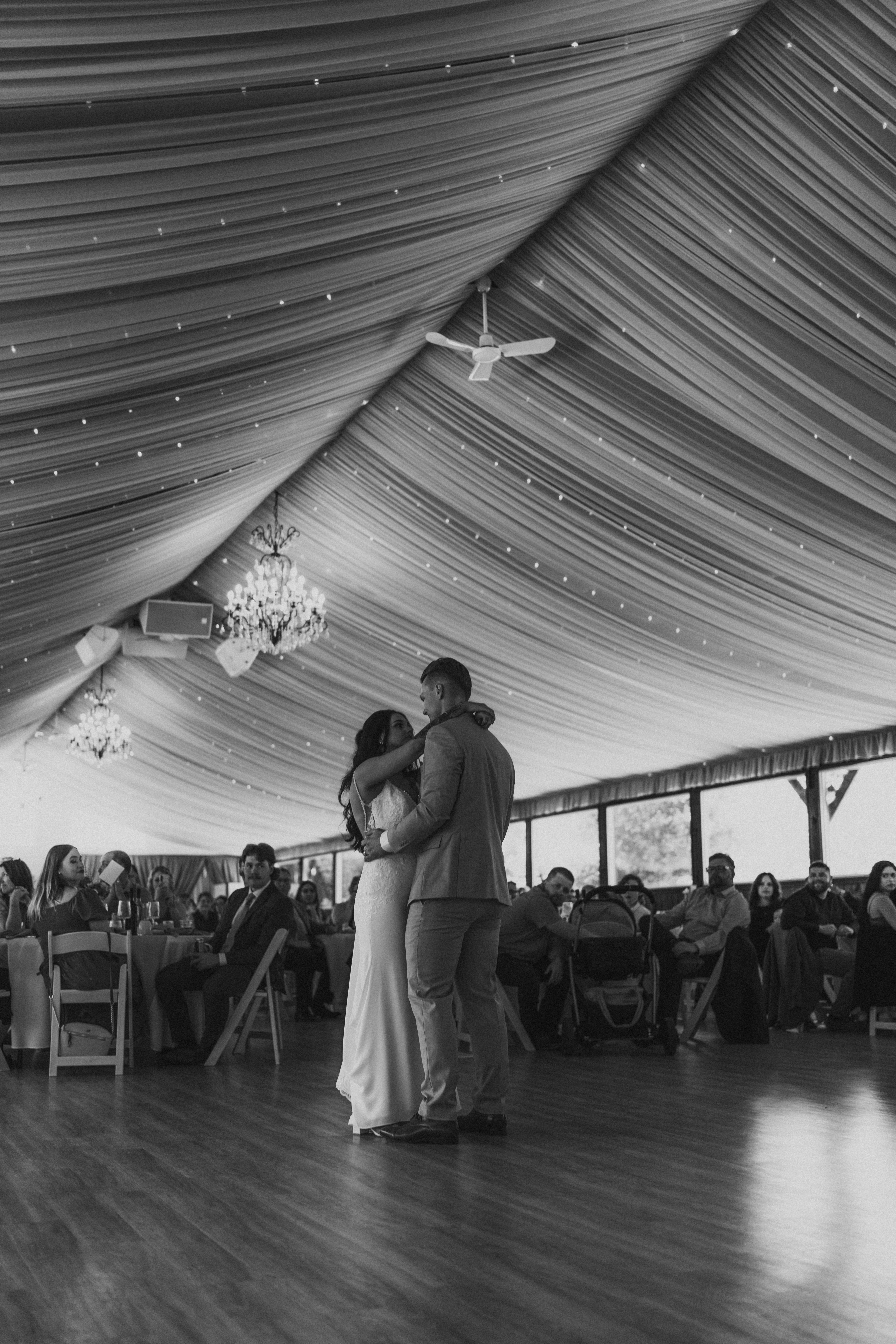 Wide interior shot of the Ashgrove Acres reception tent showing white draped ceiling, chandeliers, and guests during first dance — venue photography by Chris Ngo