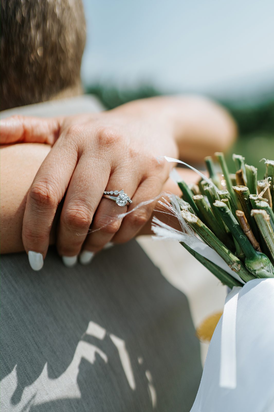 Engagement ring close-up on Christina's hand with bouquet stems — Pelican Yacht Club wedding, Ninette, Manitoba