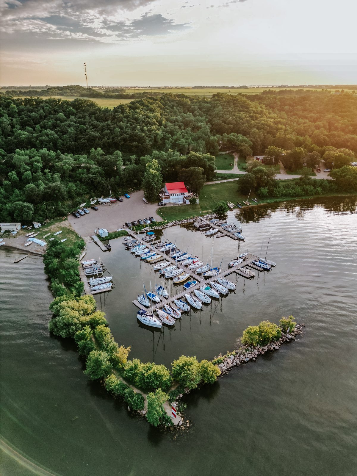 Evening aerial drone approaching the Pelican Yacht Club marina — rows of sailboats, Pelican Lake at dusk — Ninette, Manitoba
