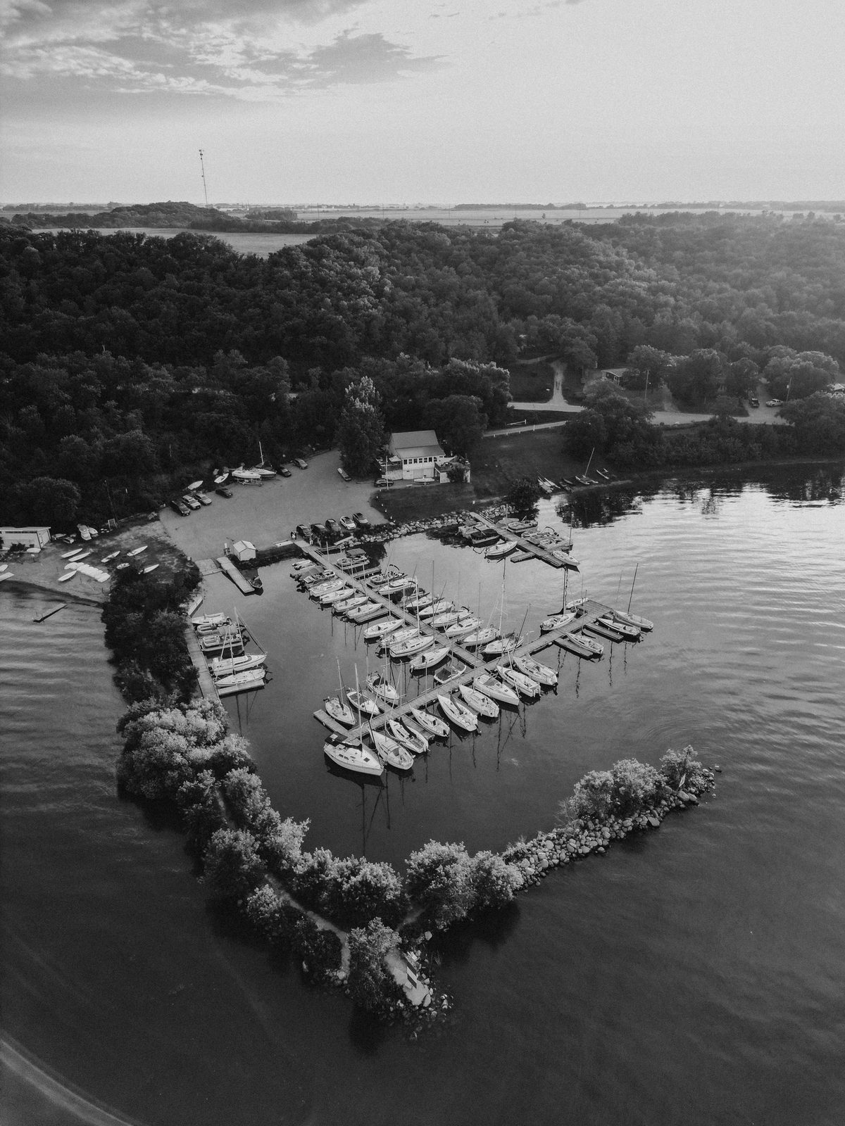Aerial drone shot — Christina and Jack lying on the marina dock between sailboats at Pelican Yacht Club, teal water on both sides — Ninette, Manitoba wedding photographer Chris Ngo