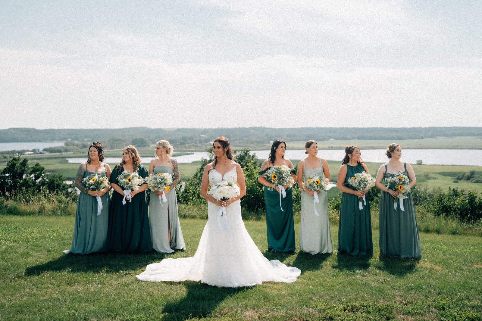 Bridesmaids in mismatched green dresses standing with Pelican Lake behind them, film-toned — Pelican Yacht Club wedding, Ninette, Manitoba