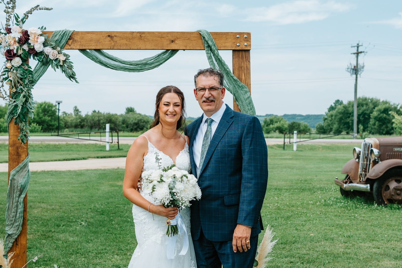 Christina with her father in a navy plaid suit at the Pelican Yacht Club arbor, antique red truck visible in the background — Ninette, Manitoba