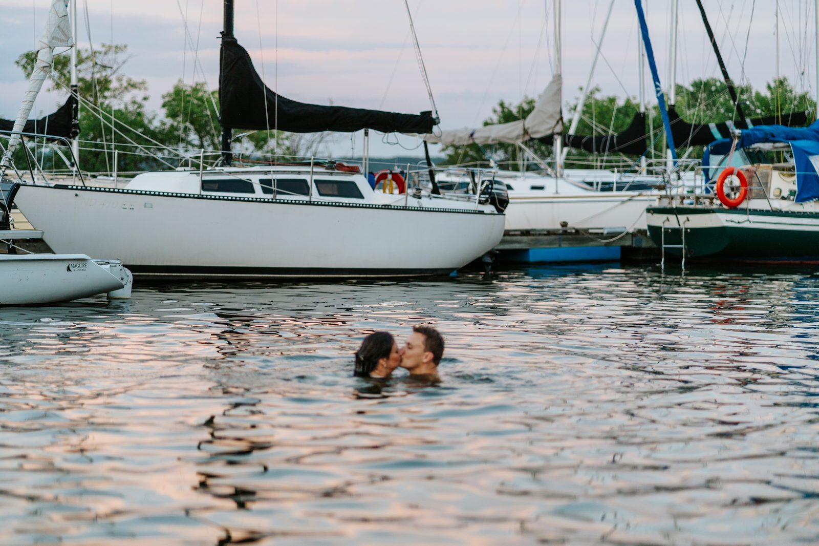 Christina and Jack kissing in the water at the Pelican Yacht Club marina, shoulder-deep between sailboats — Ninette, Manitoba