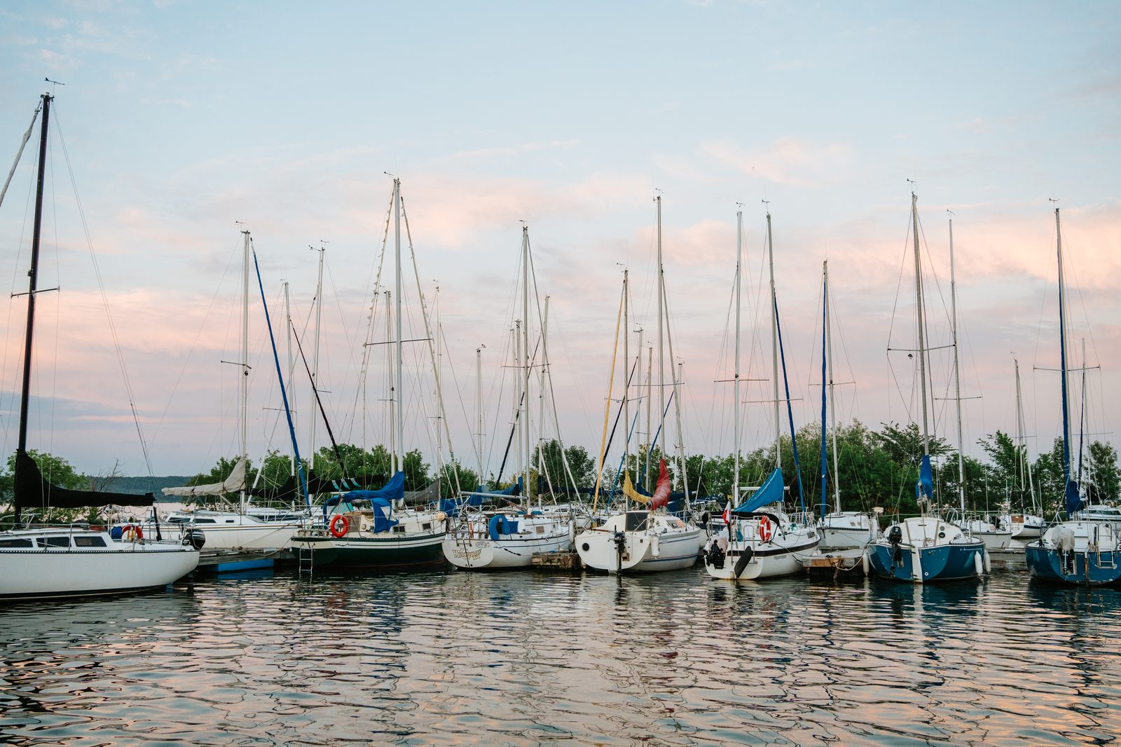 Pelican Yacht Club marina at golden hour — rows of sailboats moored at the dock, pink and purple sky reflected in still water — Ninette, Manitoba wedding photography
