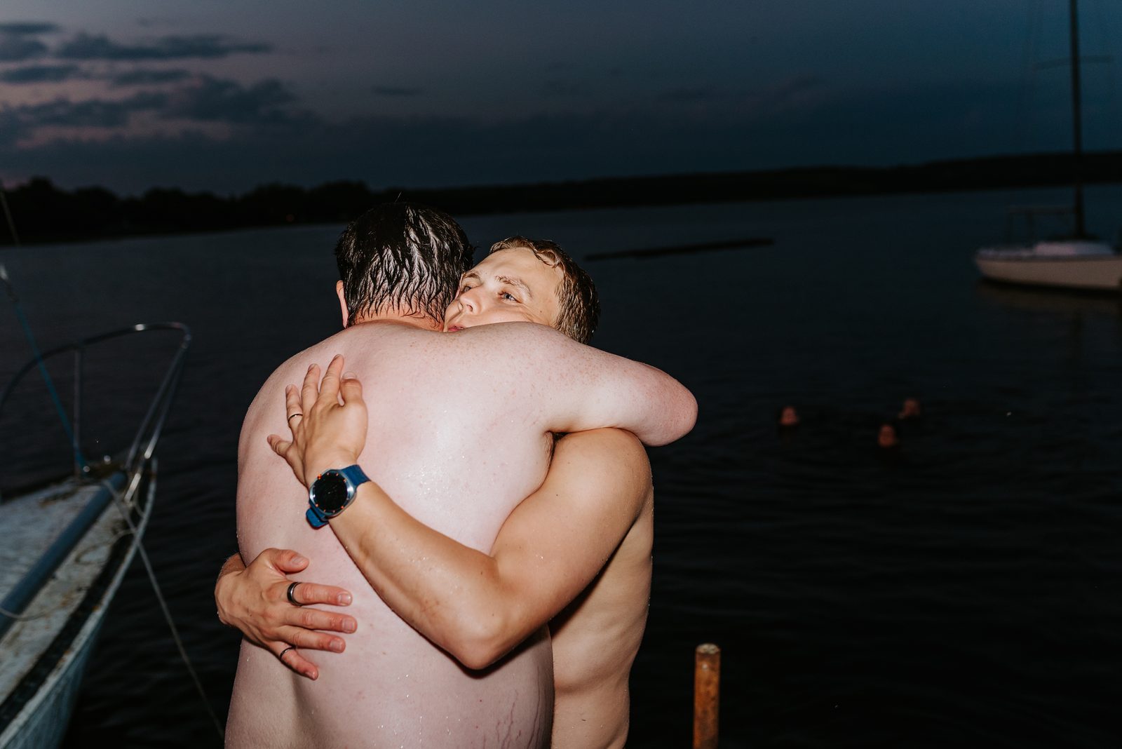 Jack and groomsman hugging on the dock at blue hour, sailboat behind them — Pelican Yacht Club, Ninette, Manitoba