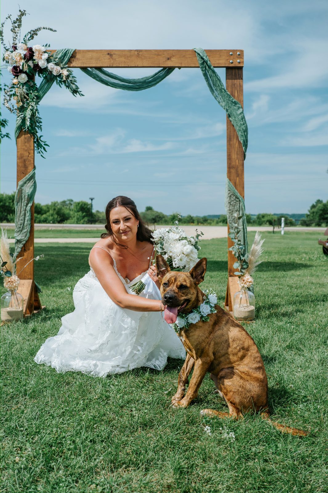 Bride Christina with their brindle Belgian Malinois mix wearing a white floral collar at the Pelican Yacht Club arbor — Ninette, Manitoba wedding photographer Chris Ngo