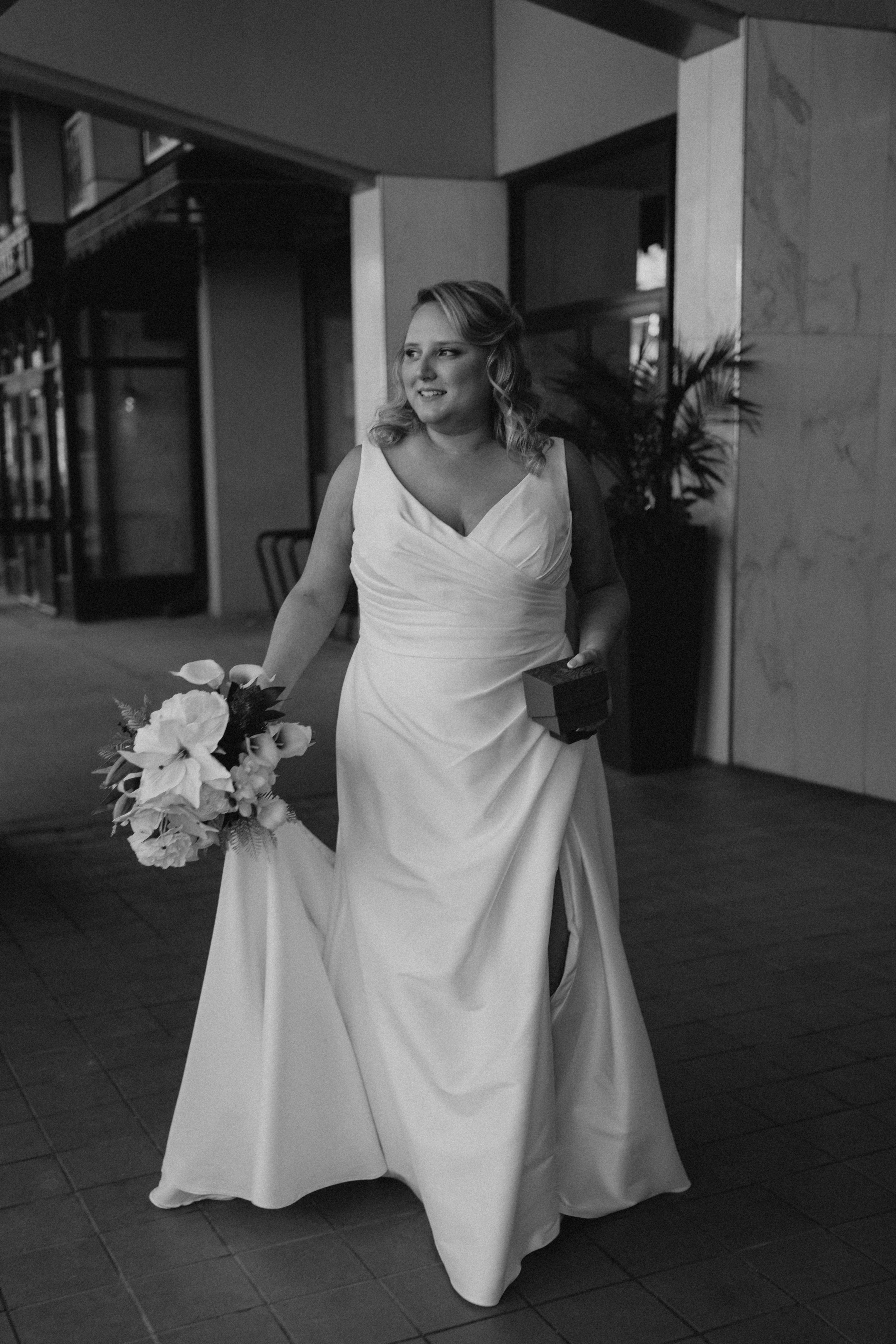 Bailey walking in her V-neck wedding gown on the streets of downtown Winnipeg before the reception at Rudy's — Ngo Photography