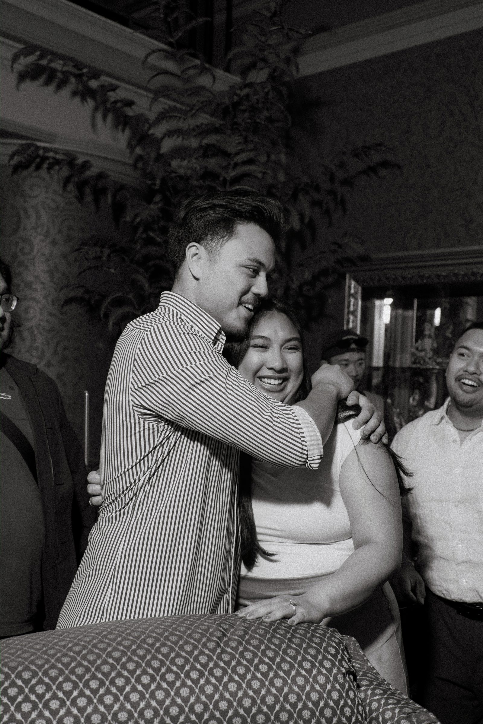 Friends embracing Annie after Deril proposed — candid black and white photography inside a historic downtown Winnipeg space — Ngo Photography