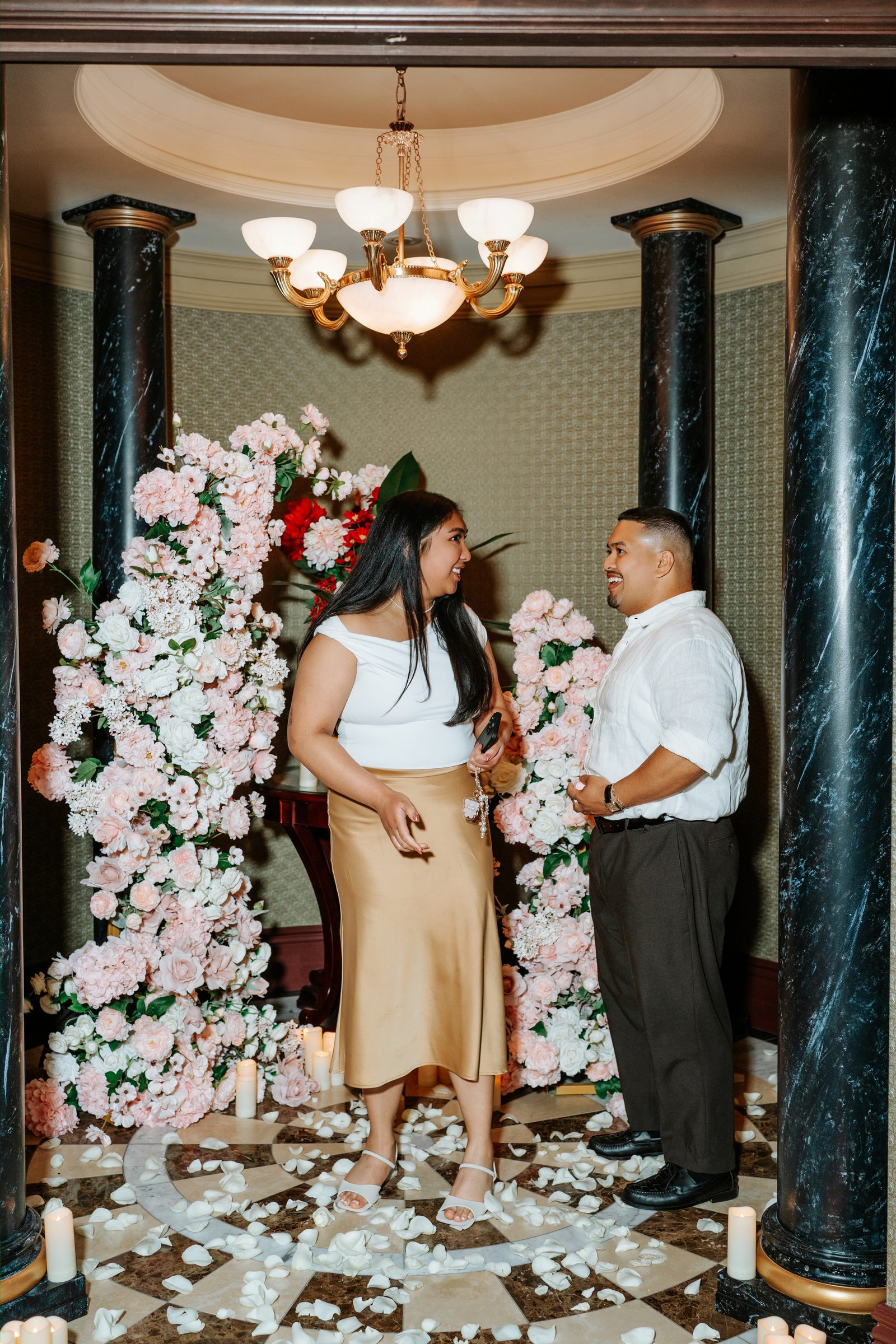 Deril holding Annie's hand with the candles and marble floor behind them — proposal moment in a private historic space downtown Winnipeg — Chris Ngo photographer