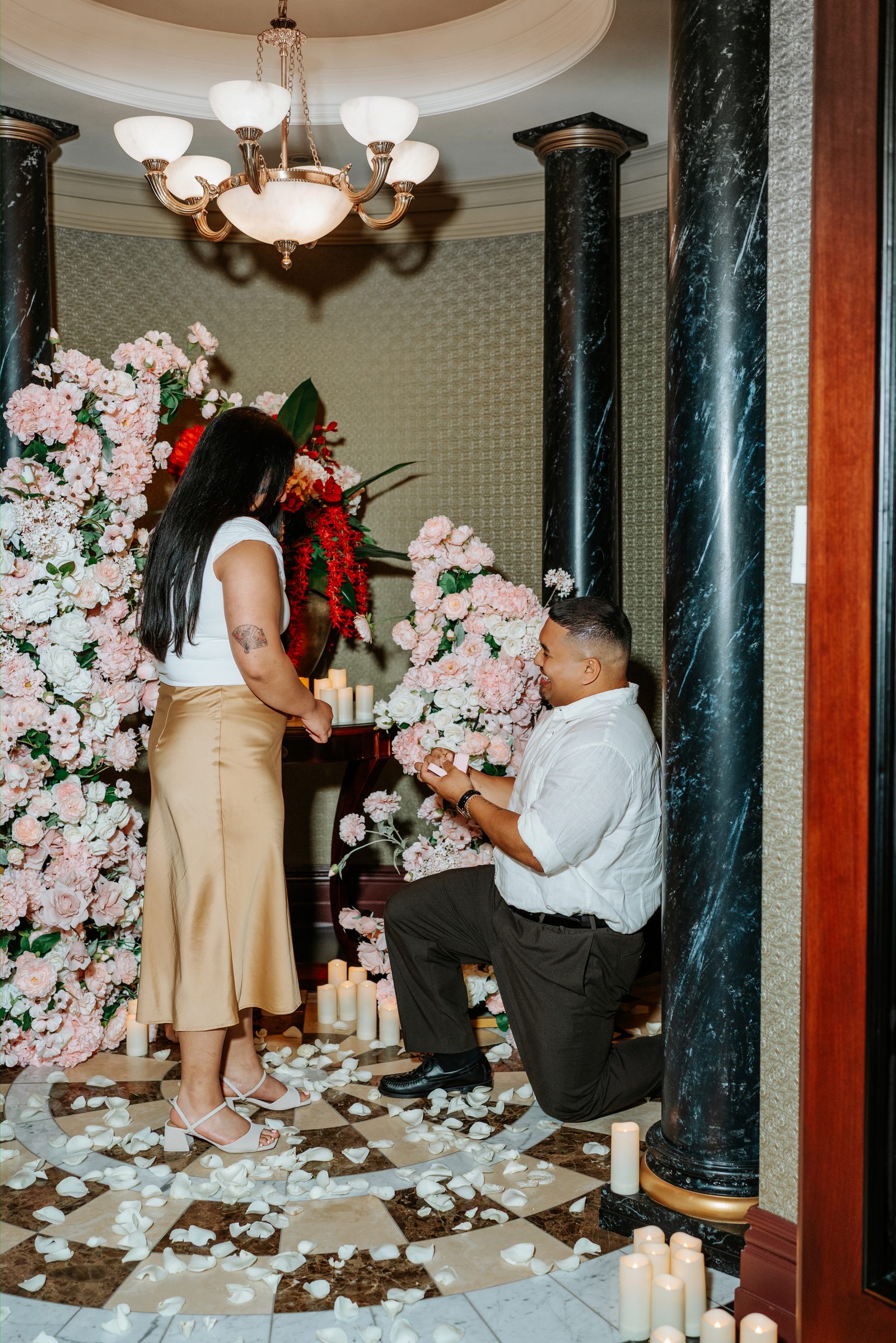 Annie and Deril embracing in front of the floral arches after the proposal — wide view with marble floor and chandelier above — surprise proposal photography downtown Winnipeg by Chris Ngo