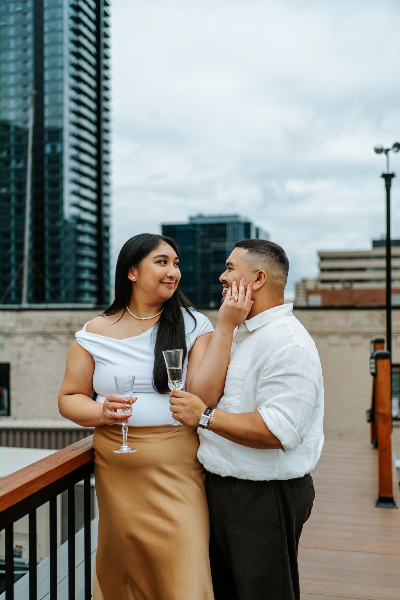 Annie and Deril close portrait on the rooftop terrace with downtown Winnipeg buildings behind them — proposal photographer Chris Ngo