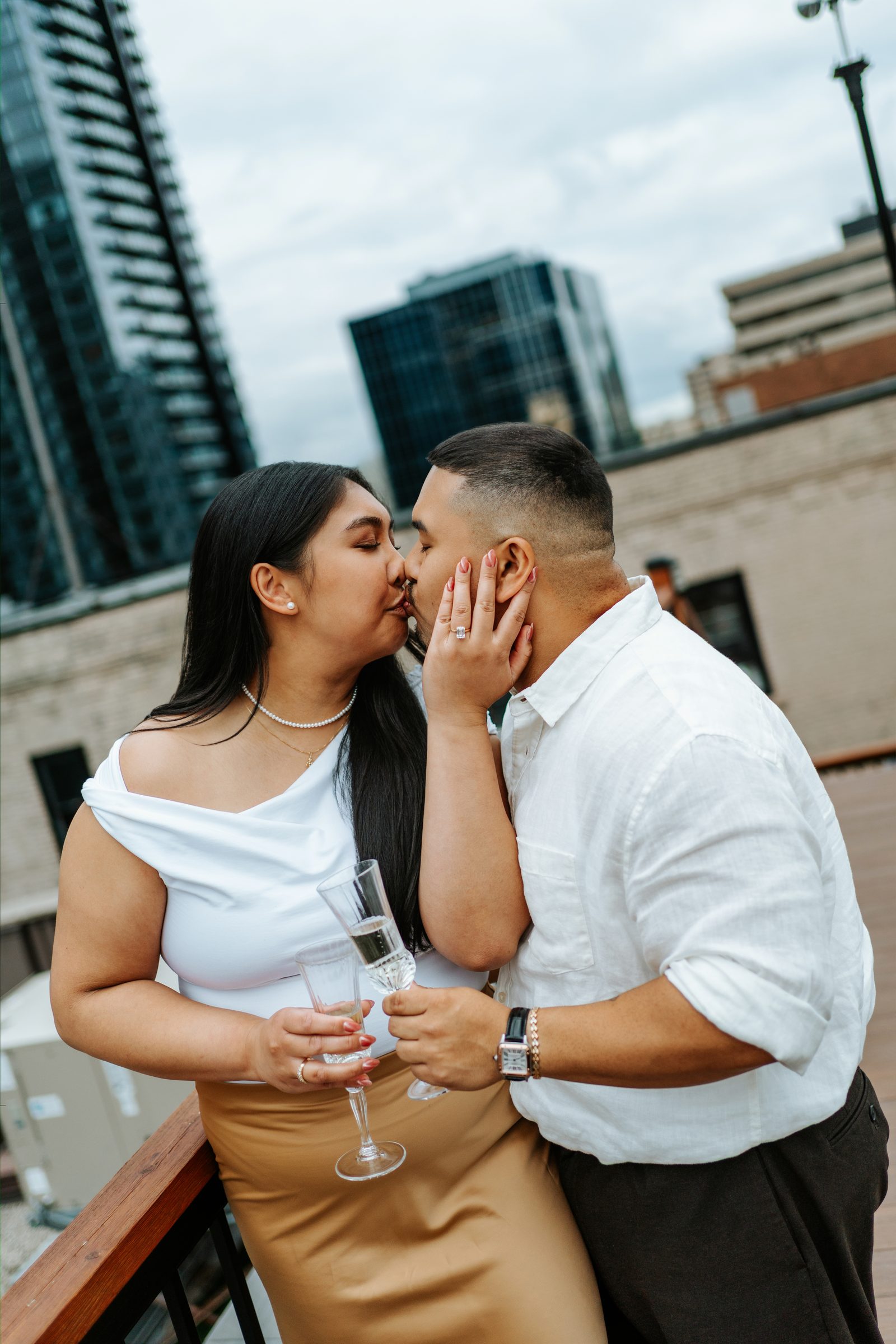 Deril spinning Annie on the rooftop deck with the Winnipeg skyline and a white angel sculpture — just engaged — proposal photography by Chris Ngo Ngo Photography