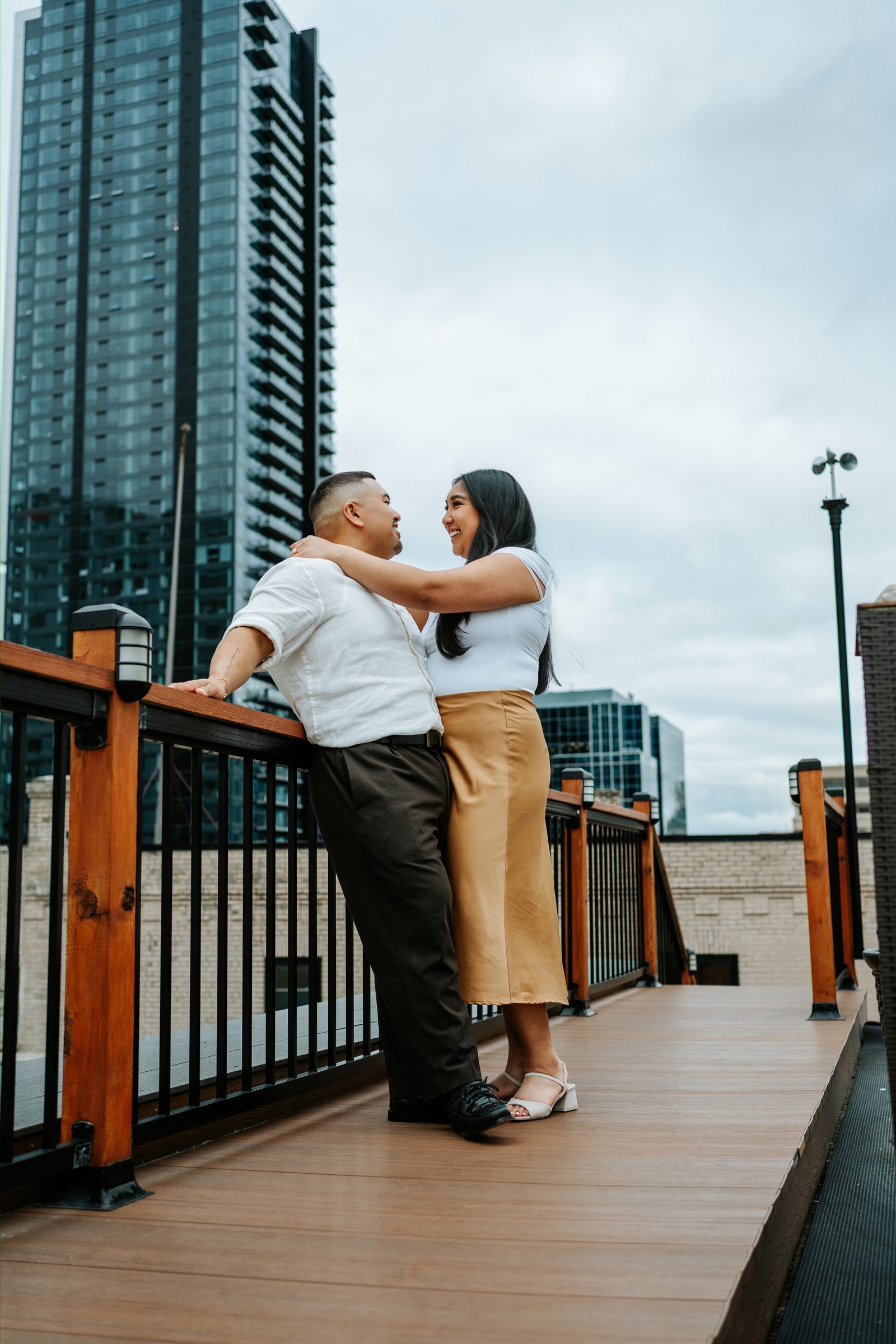 Deril and Annie close portrait leaning against the rooftop railing with the downtown Winnipeg skyline — surprise proposal photography by Chris Ngo Ngo Photography