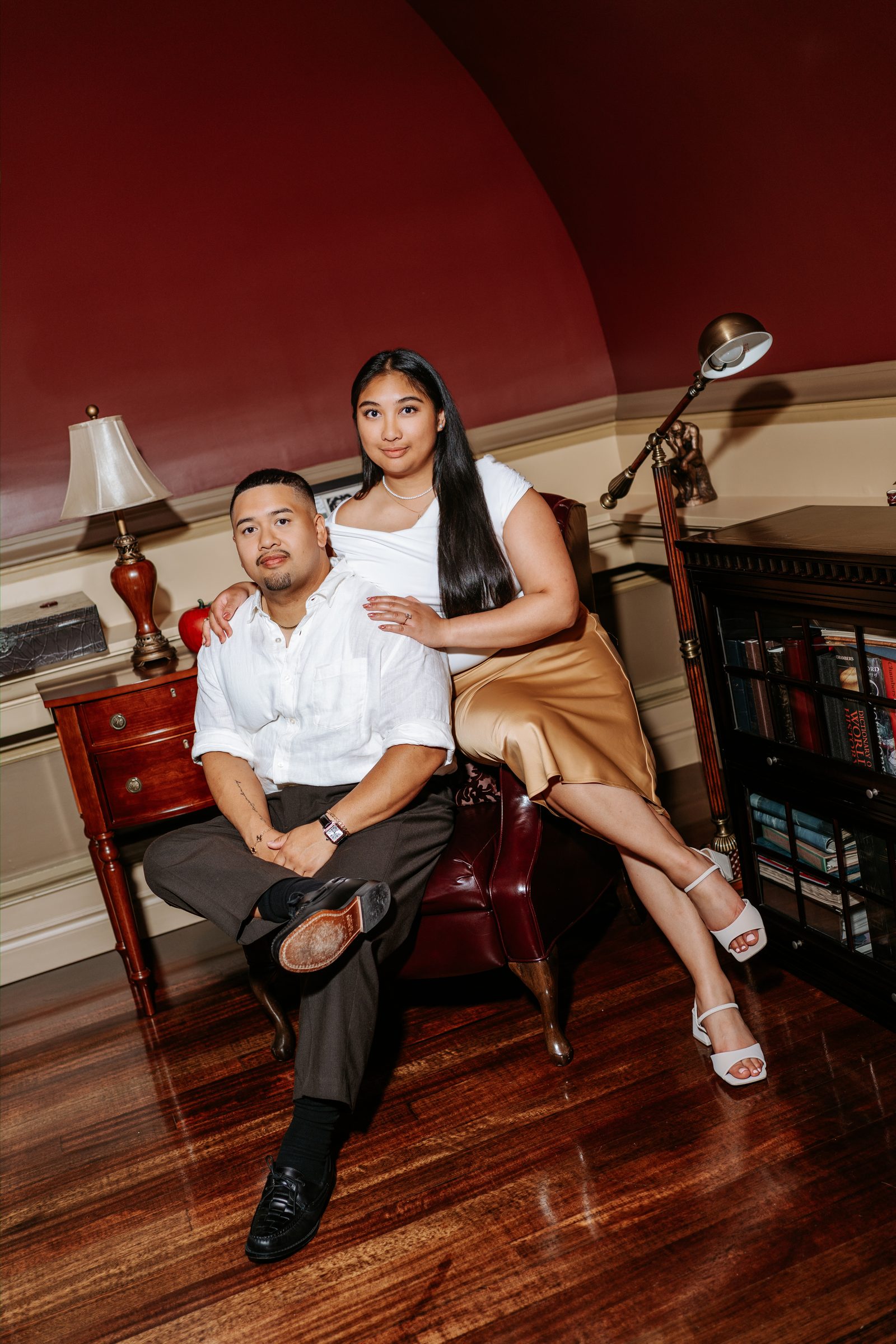 Deril and Annie posed portrait on the rooftop terrace steps with a marble classical statue and downtown Winnipeg buildings — surprise proposal photography by Chris Ngo