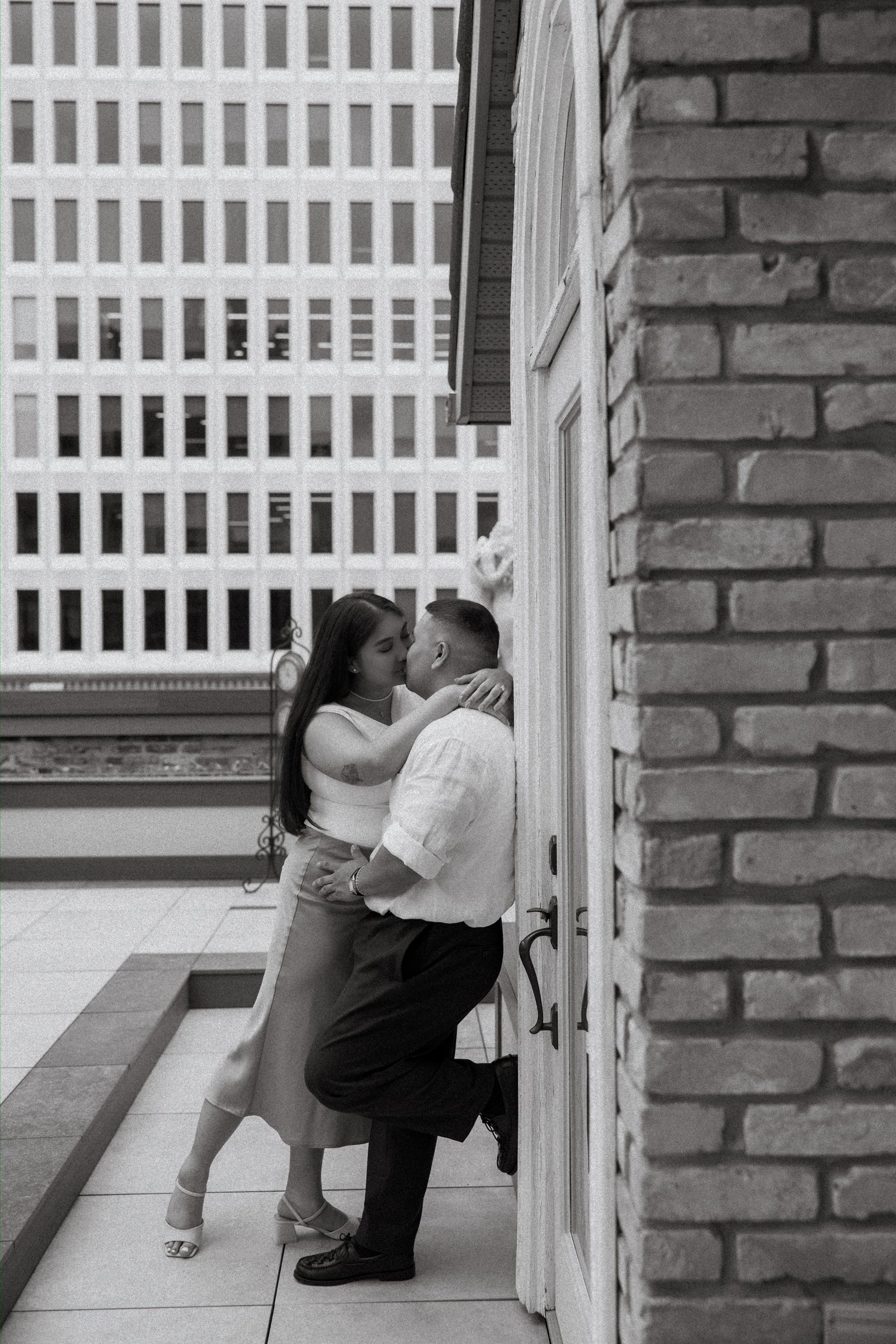 Wide portrait of Annie and Deril on the rooftop of a private historic space in downtown Winnipeg — city skyline behind them — just engaged — proposal photography by Chris Ngo Ngo Photography