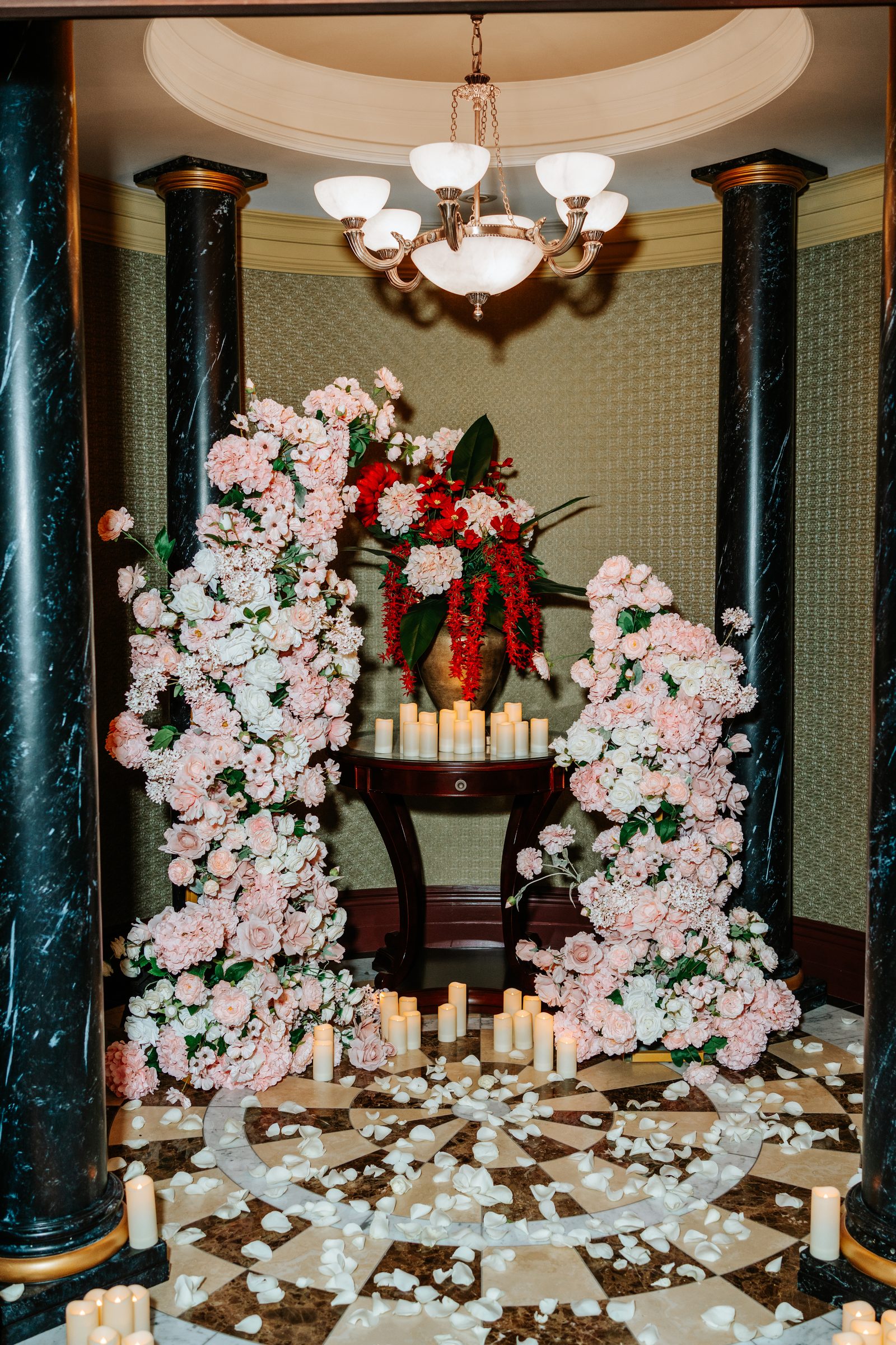 Twin floral arches of blush garden roses and peonies flanking a marble table with candles and rose petals on the marble floor — proposal setup in a private historic space in downtown Winnipeg by Ngo Photography