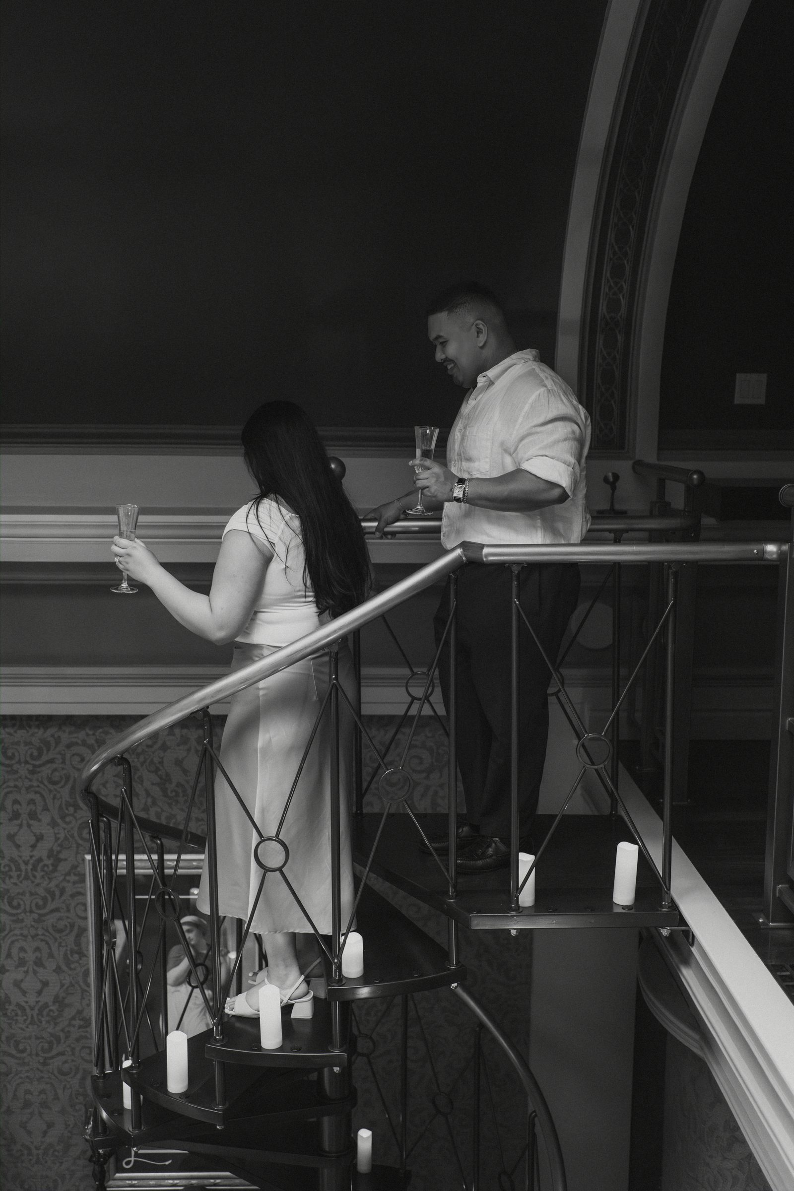 Deril and Annie on the ornate wrought-iron staircase with candles on every step — black and white portrait in a private historic space in downtown Winnipeg — proposal photography by Chris Ngo Ngo Photography