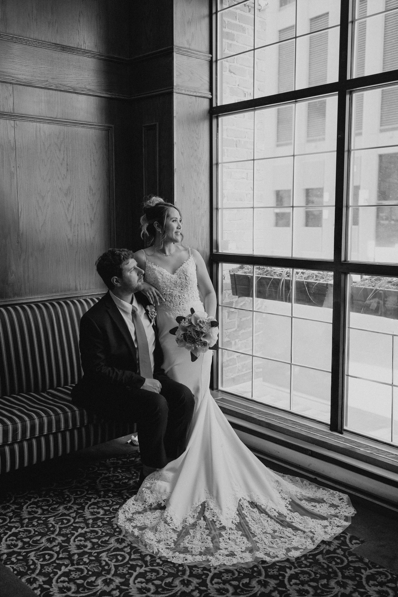 Justin standing by window, Eden seated on sofa at Bailey's Restaurant wedding — Ngo Photography Winnipeg