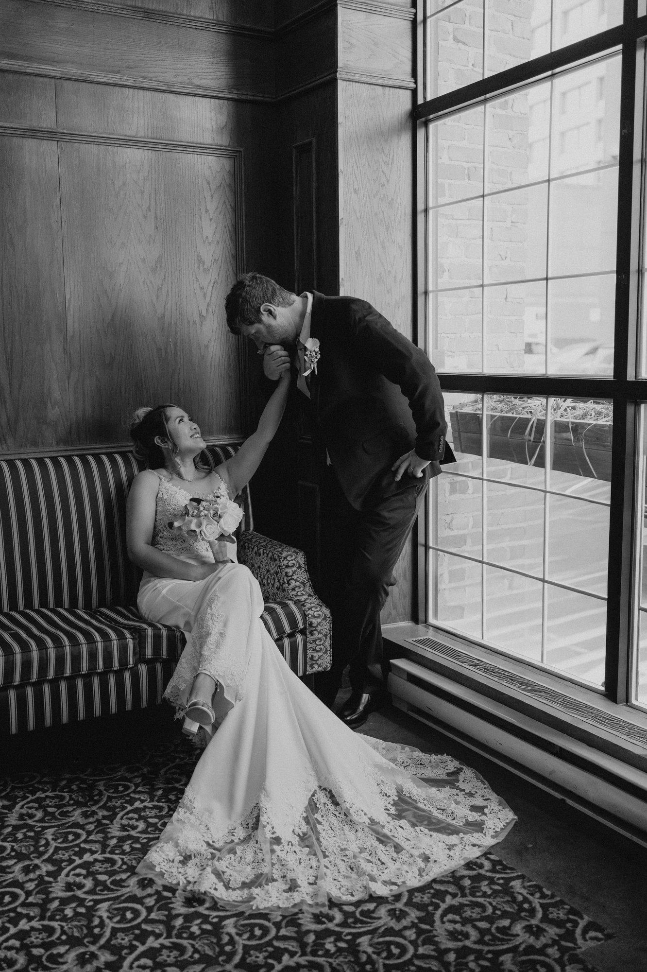Eden and Justin laughing together by the large industrial windows at Bailey's Restaurant Winnipeg — wedding photography by Chris Ngo