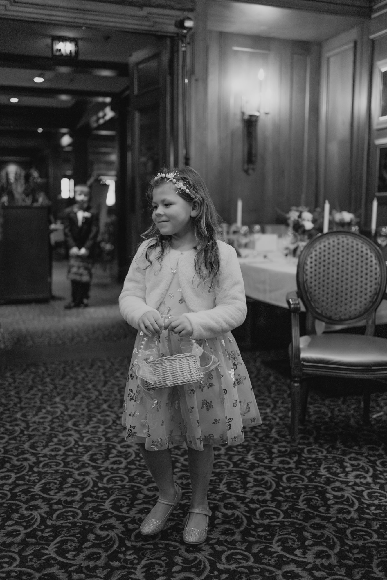 Flower girl in black dress and floral crown wandering the ornate dining room at Bailey's Restaurant Winnipeg — wedding photography by Chris Ngo, Ngo Photography