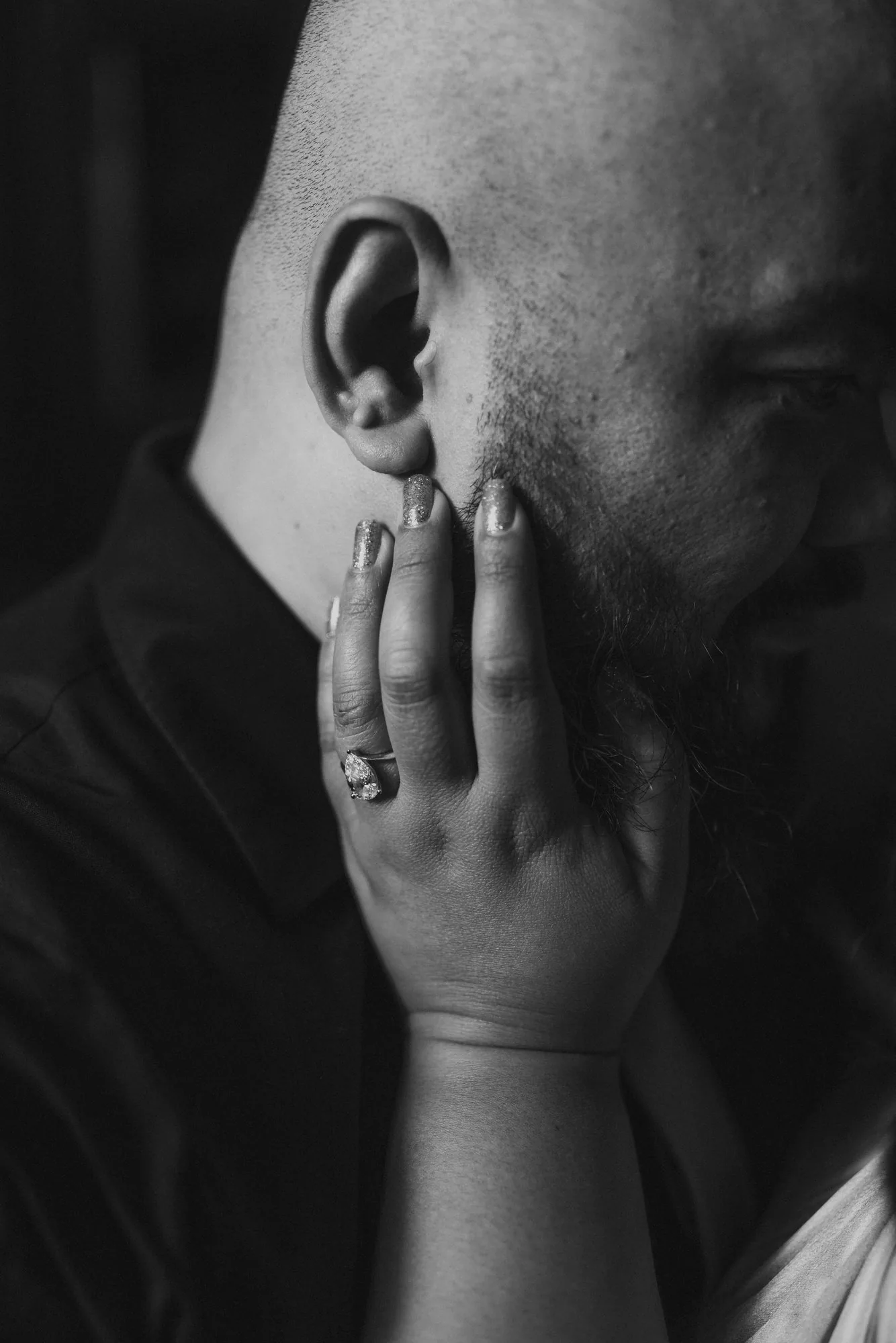 Black and white close-up of fiancée's hand with engagement ring gently cupping her partner's face — editorial engagement photography by Ngo Photography