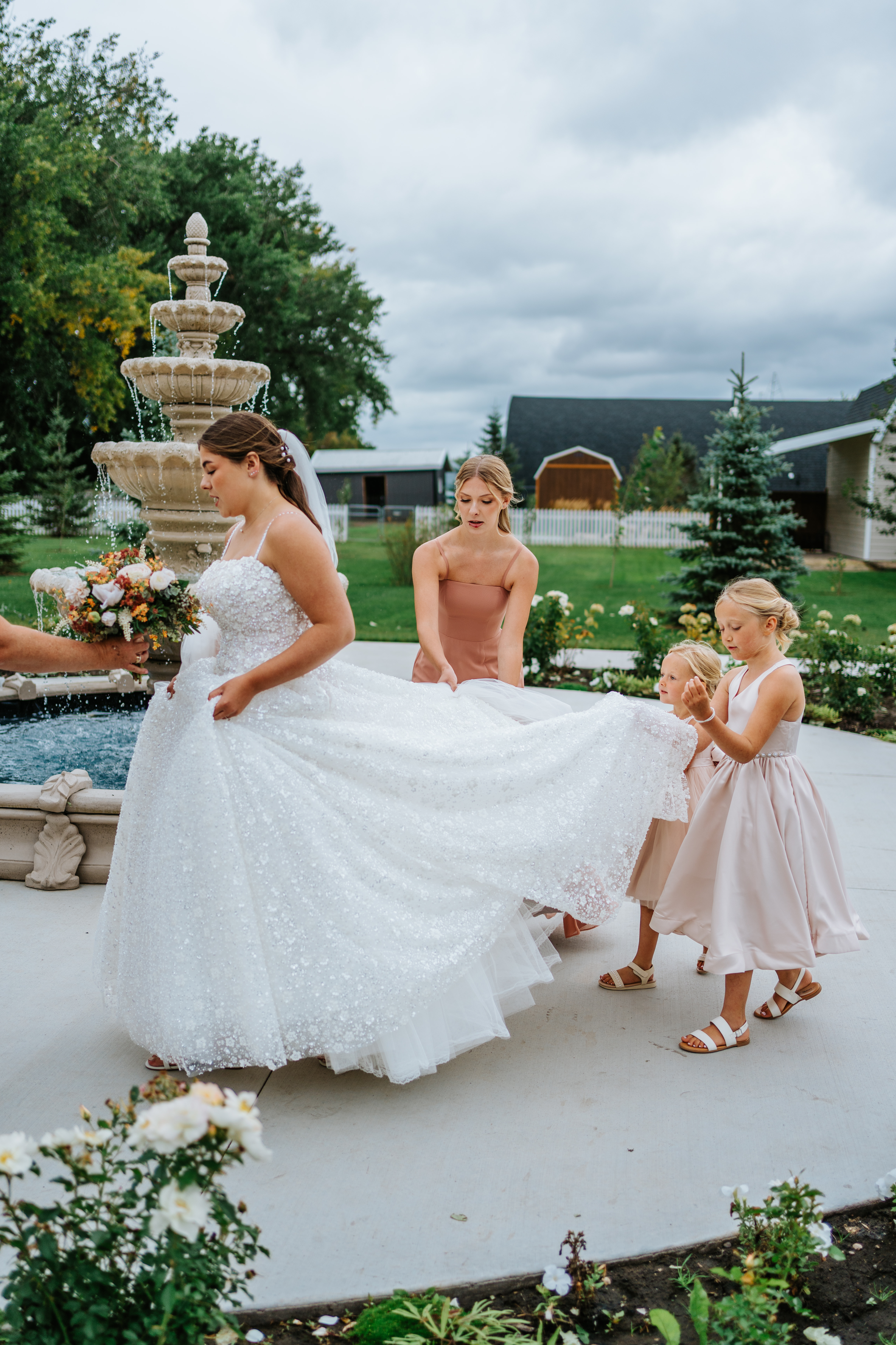 Erin in her wedding gown with the flower girls by the fountain at Buttercup Café Manitoba — candid bridal portrait by Ngo Photography