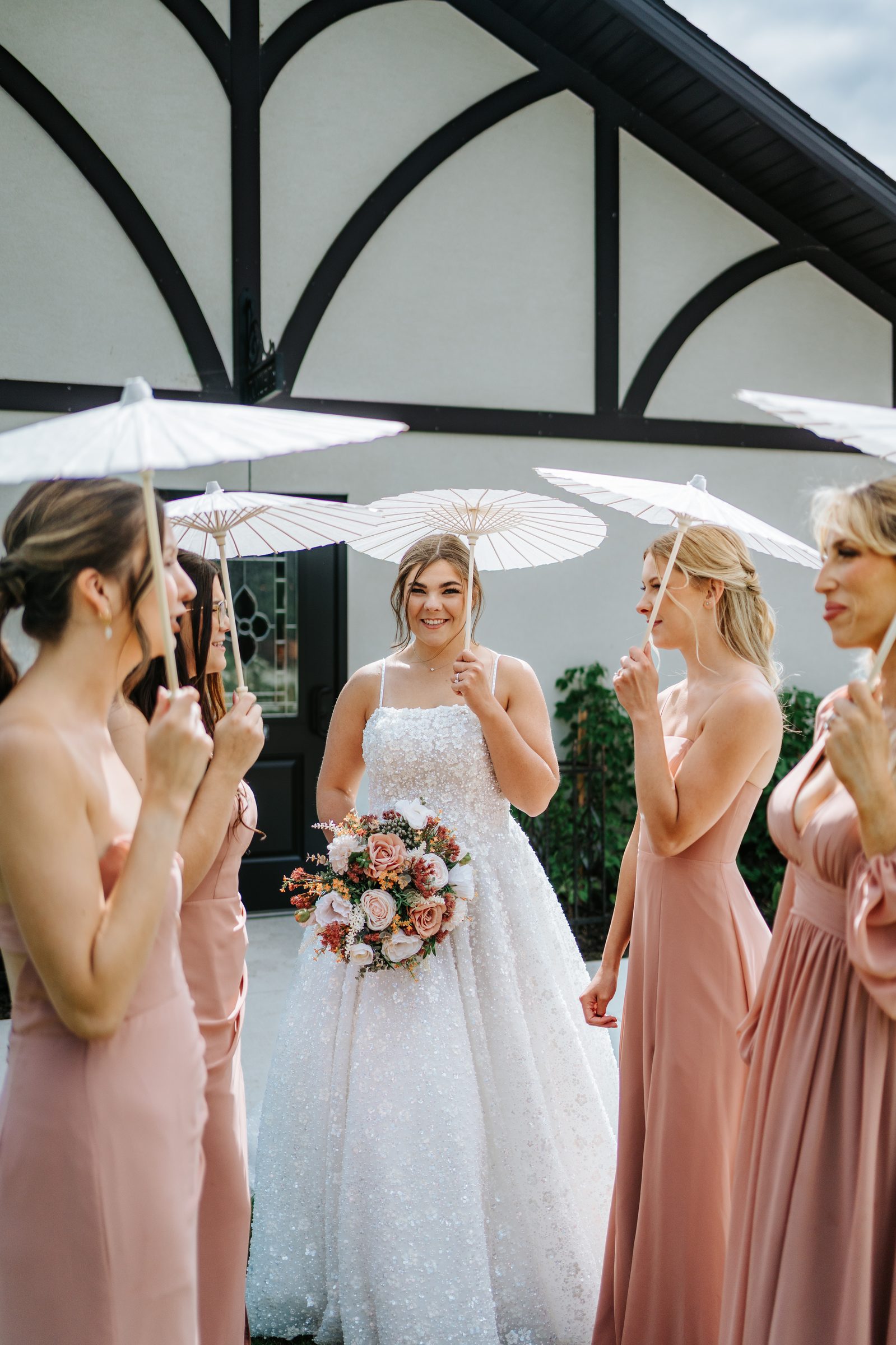 Erin with her bridesmaids holding white parasols in front of Buttercup Café — wedding party portrait by Ngo Photography Winnipeg