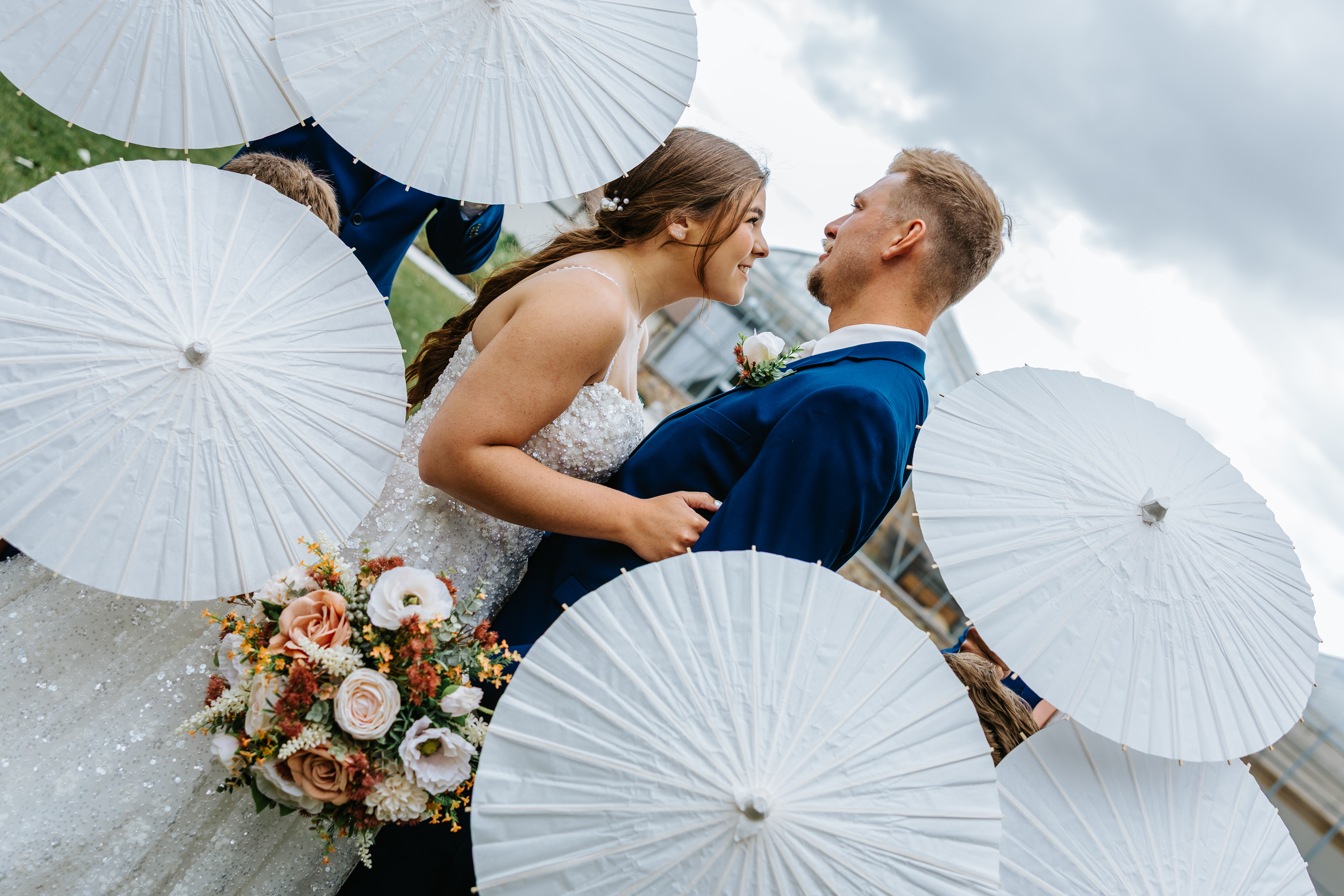 Erin and Jayden surrounded by white parasols held by the wedding party — creative couple portrait at Buttercup Café Manitoba by Ngo Photography
