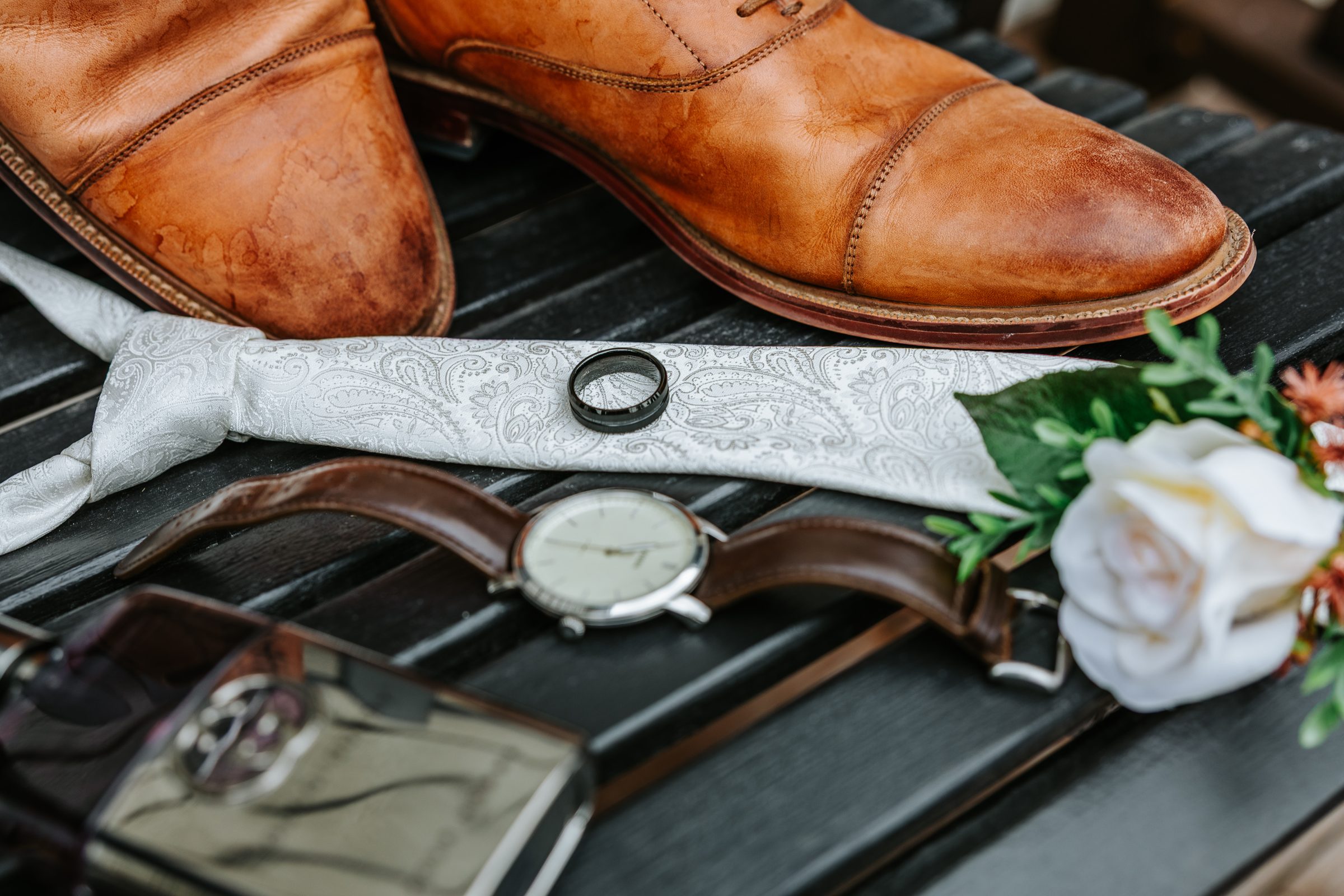 Groom details — brown leather shoes, silver paisley tie, black wedding band laid out before the Buttercup Café wedding — Ngo Photography Winnipeg