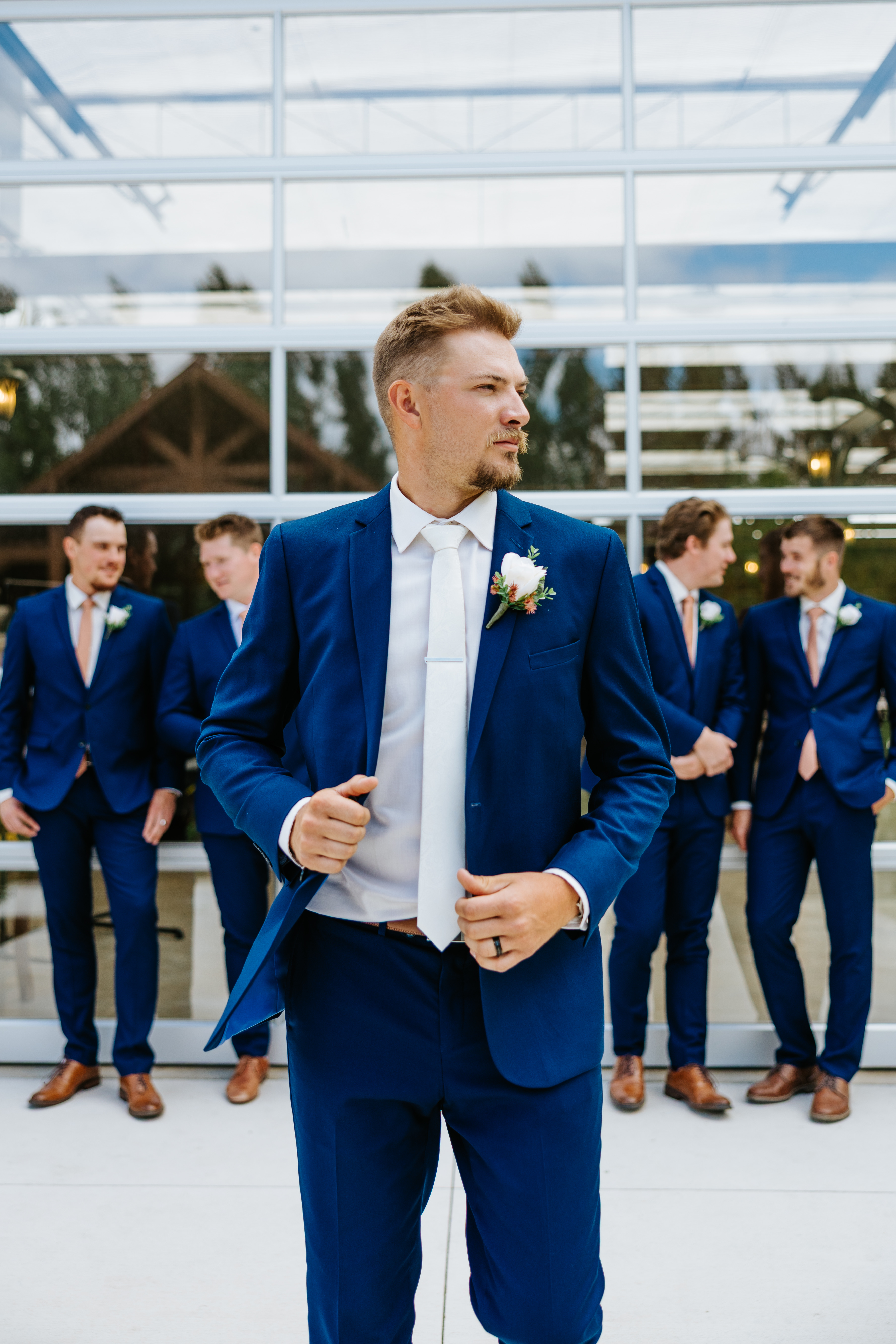Jayden in his navy suit with groomsmen lined up in front of the Buttercup Café greenhouse — groom and groomsmen portrait by Ngo Photography
