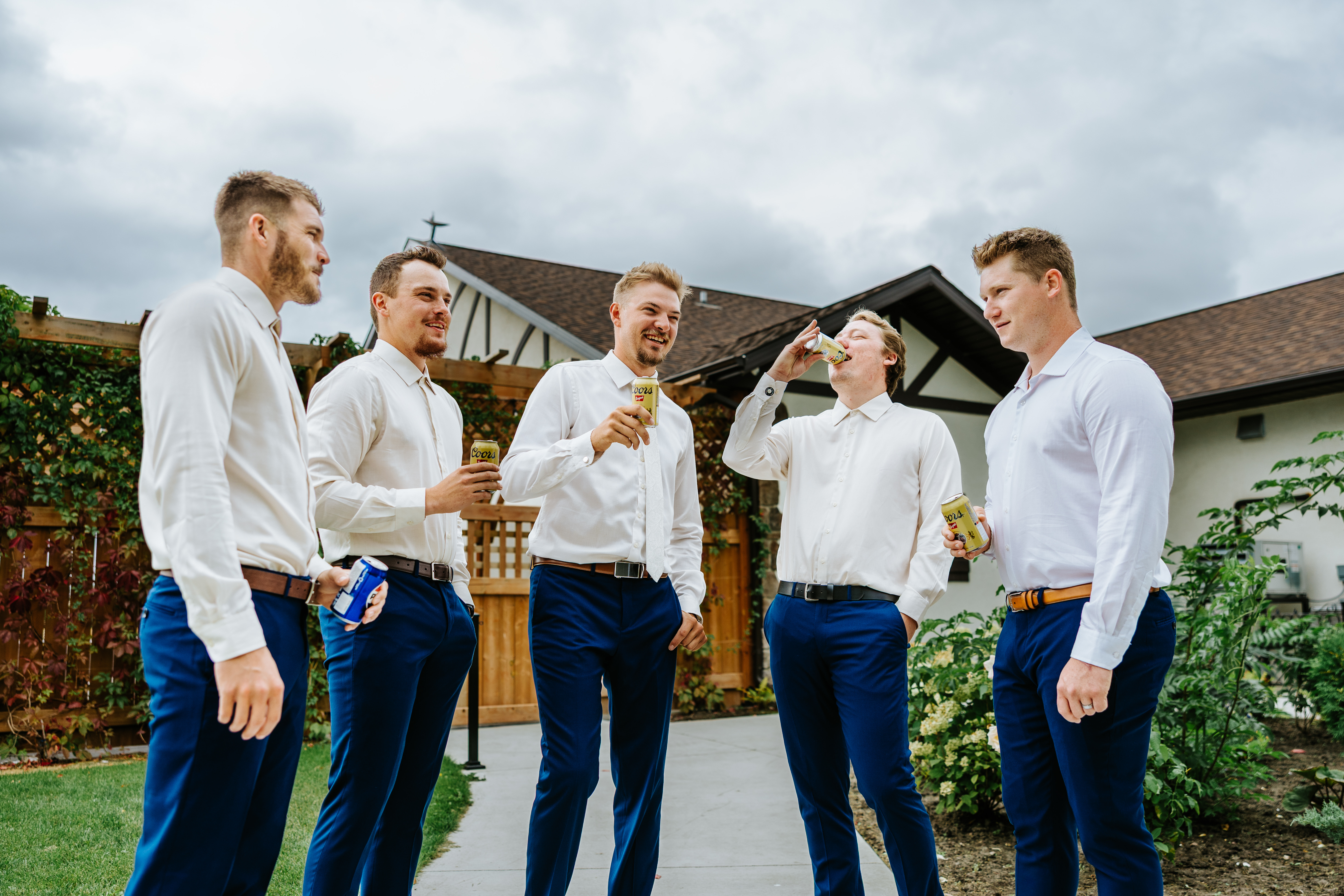 Groomsmen in white shirts and navy trousers laughing outside the Tudor building at Buttercup Café Manitoba — getting ready candids by Ngo Photography