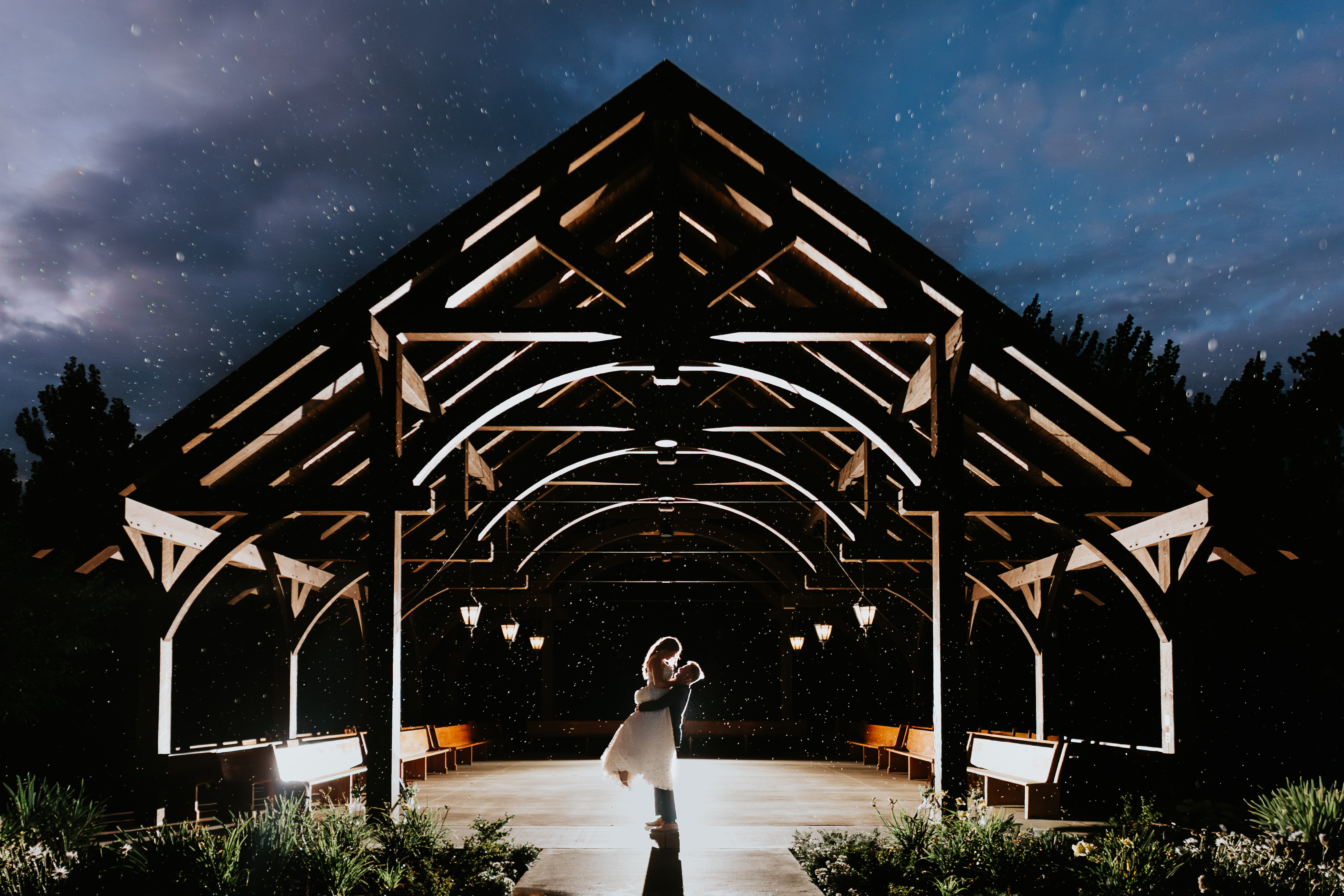 Wide night portrait of Erin and Jayden dancing in the illuminated timber pavilion at Buttercup Café with stars visible above the treeline — night wedding photography by Chris Ngo
