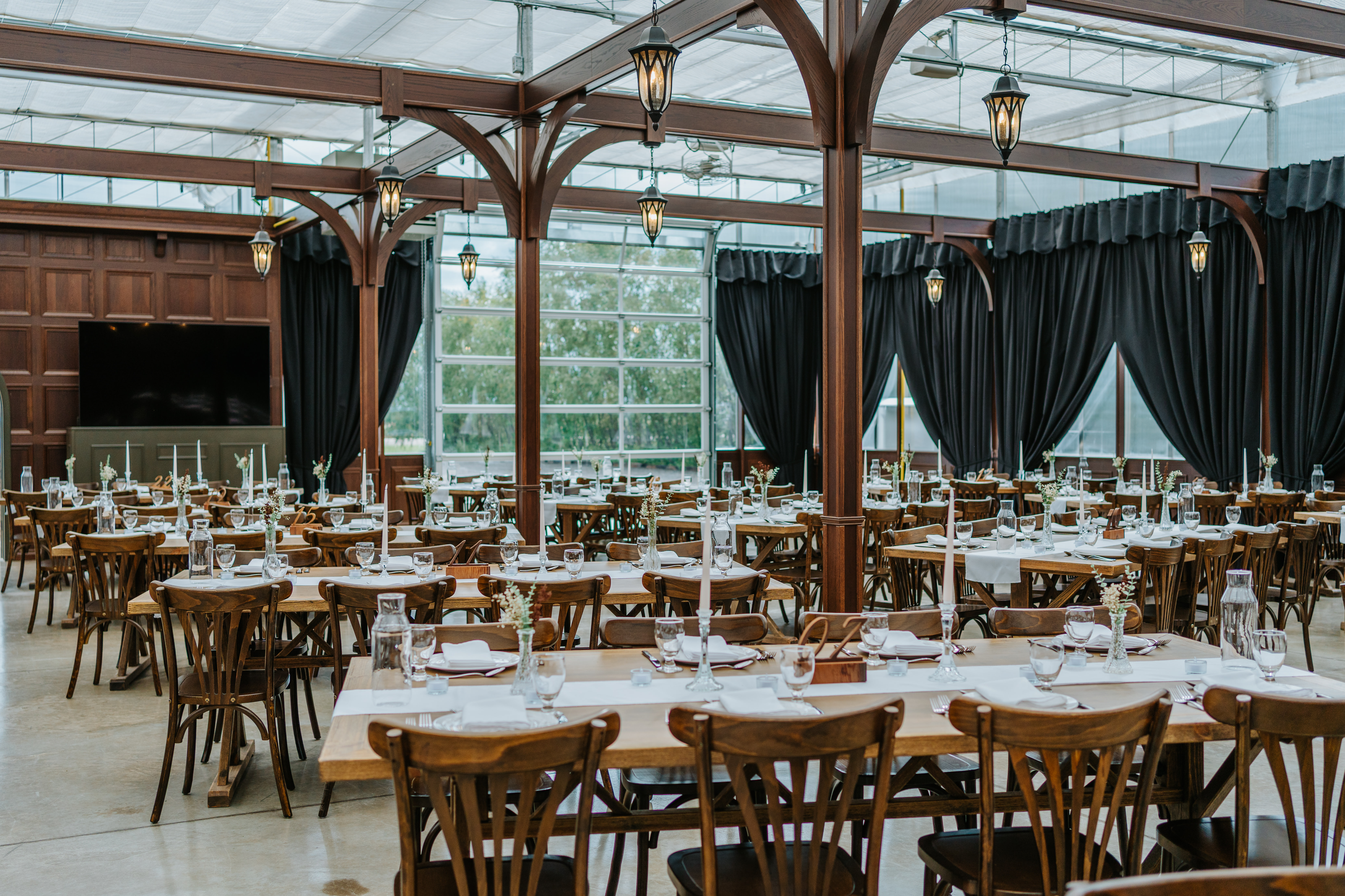 The glass greenhouse reception hall at Buttercup Café Manitoba set for dinner — round tables, pendant lanterns, floor-to-ceiling windows — wedding venue photography by Ngo Photography
