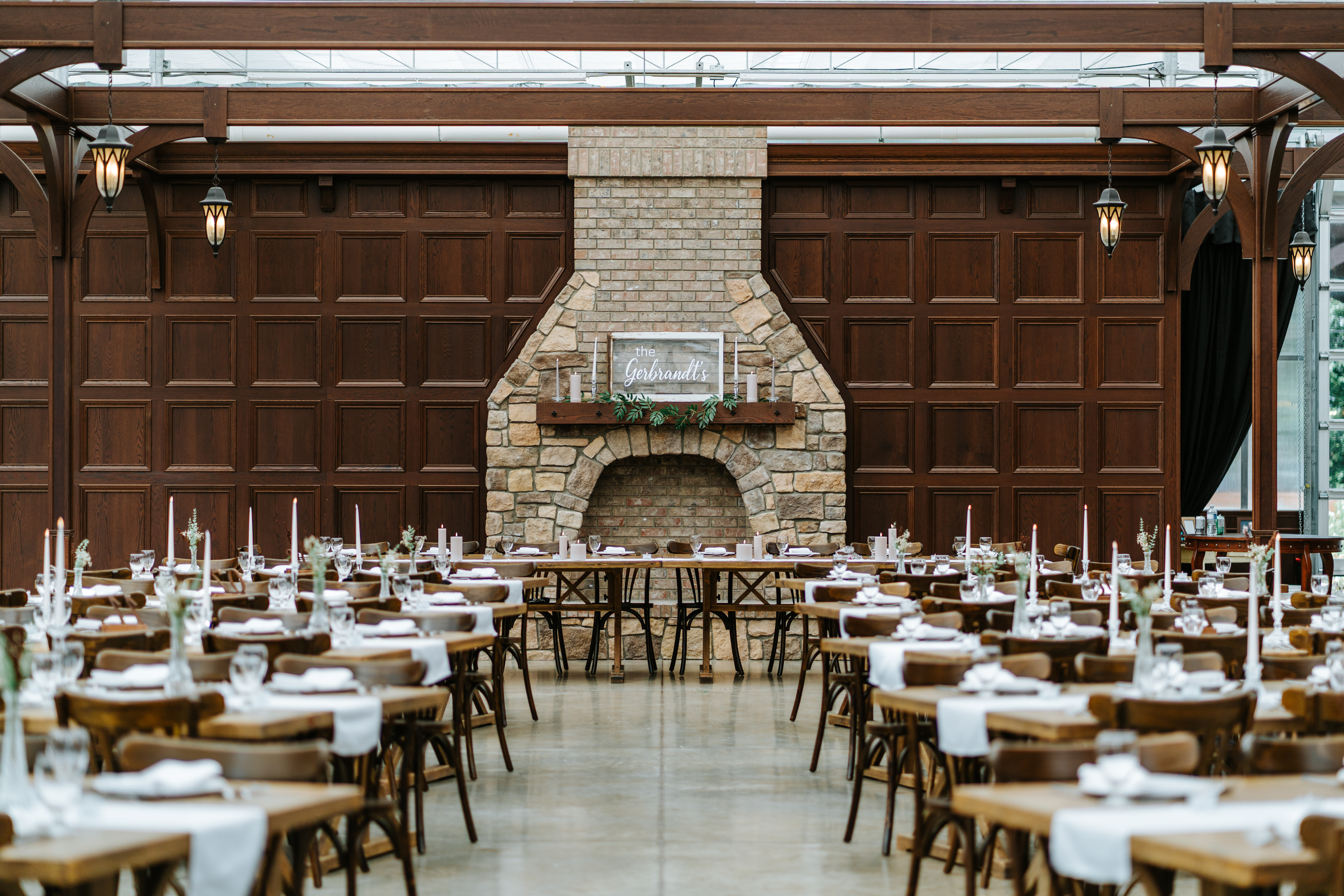 The reception hall at Buttercup Café Manitoba — stone fireplace, wooden panelling, long harvest tables set for dinner — venue photography by Chris Ngo