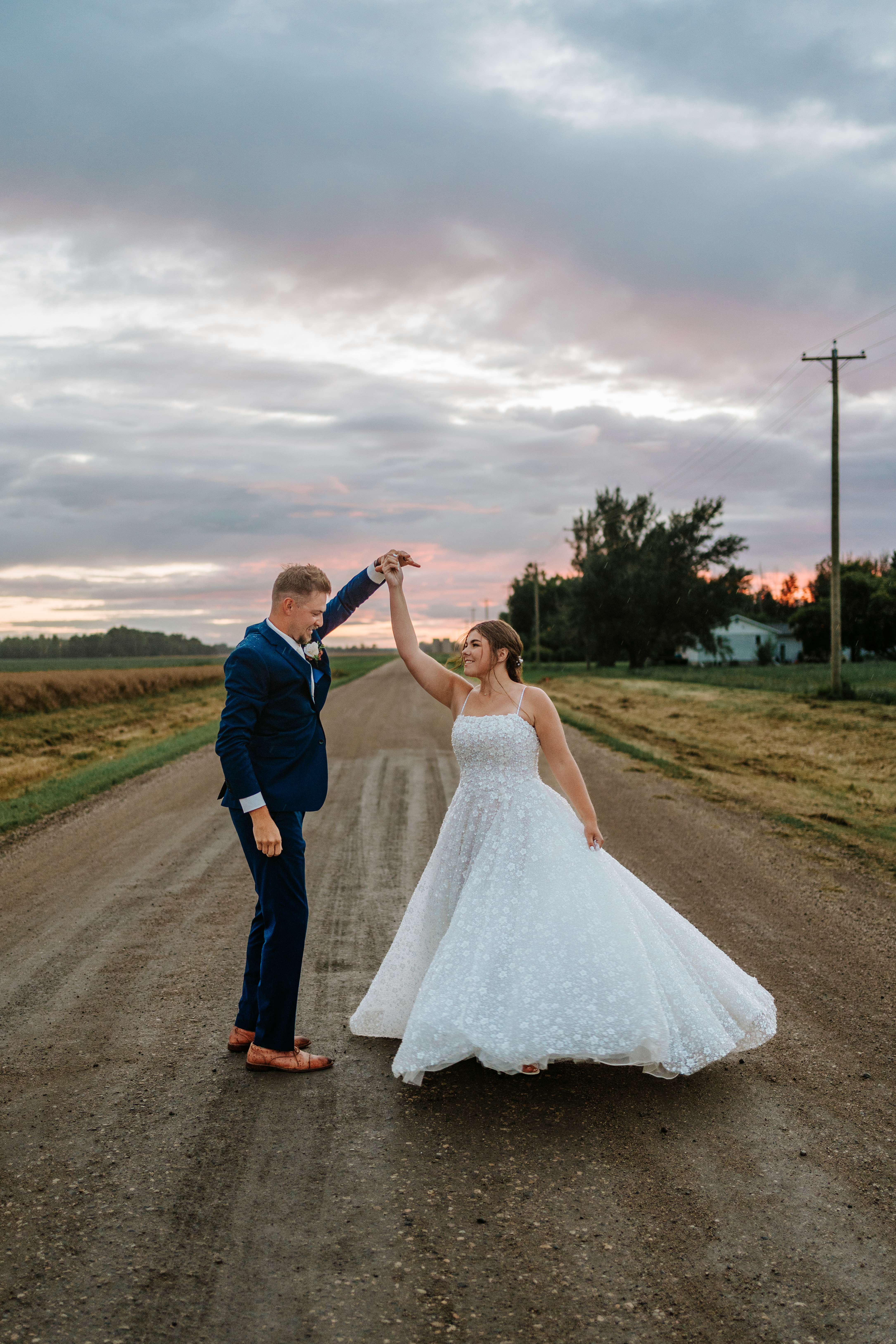 Jayden spinning Erin on a Manitoba prairie dirt road at sunset — the train of her sparkle gown lifting in the golden light — wedding portrait by Chris Ngo Ngo Photography