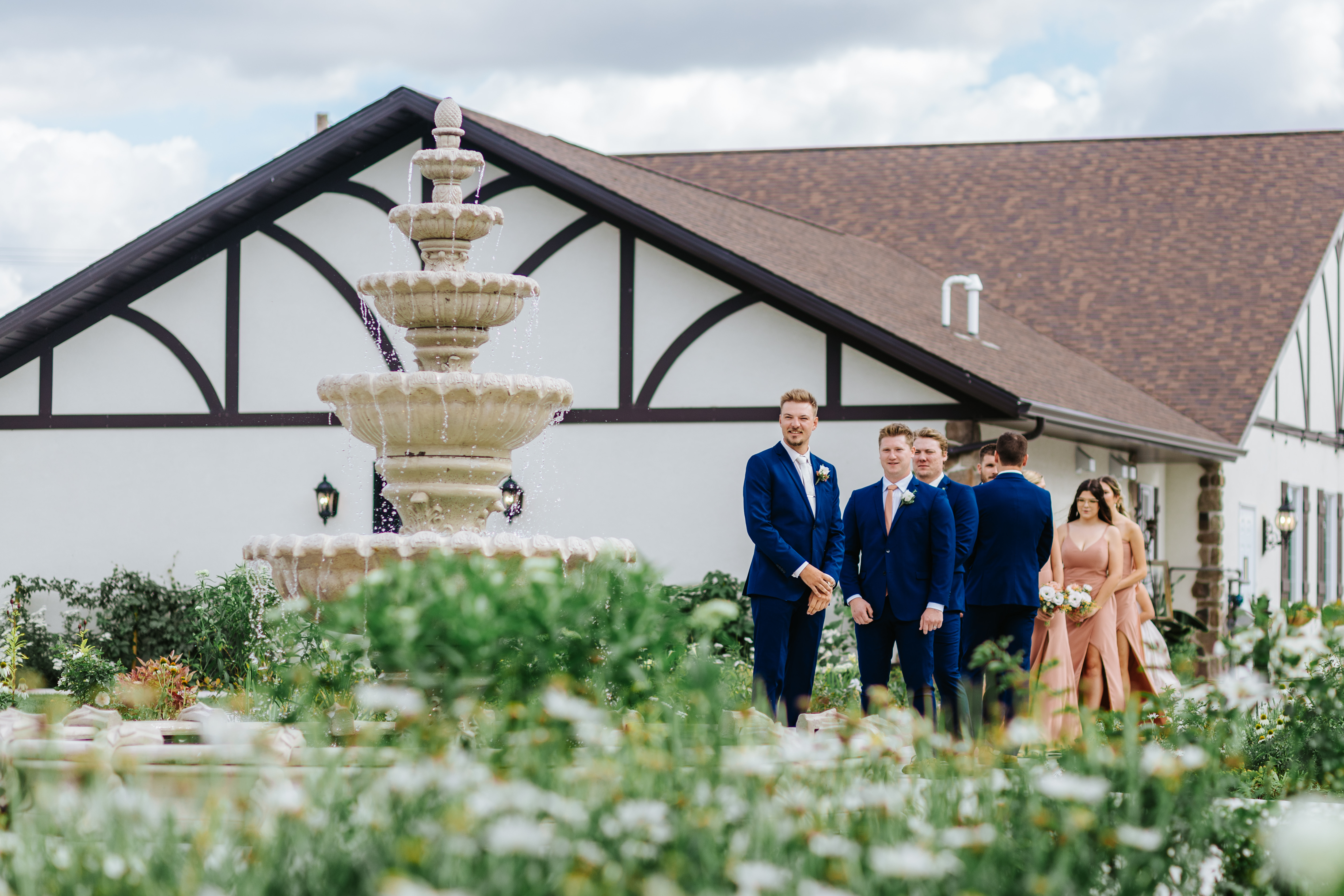 Wedding party walking through the manicured gardens past the fountain at Buttercup Café Manitoba — editorial wedding party photography by Chris Ngo