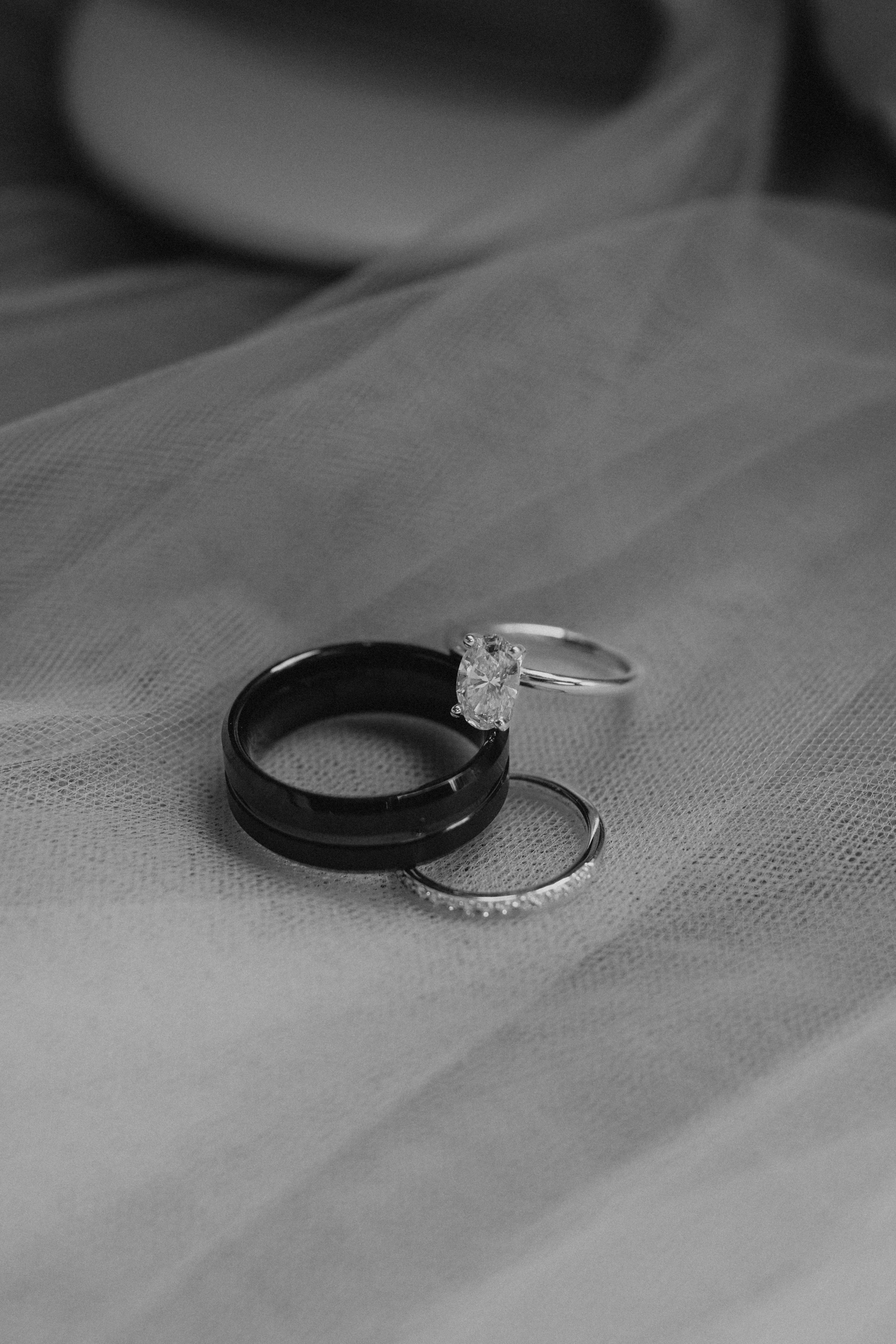 Erin and Jayden's wedding rings — matte black band, diamond solitaire and eternity ring on soft veil — Buttercup Café wedding detail photography by Ngo Photography