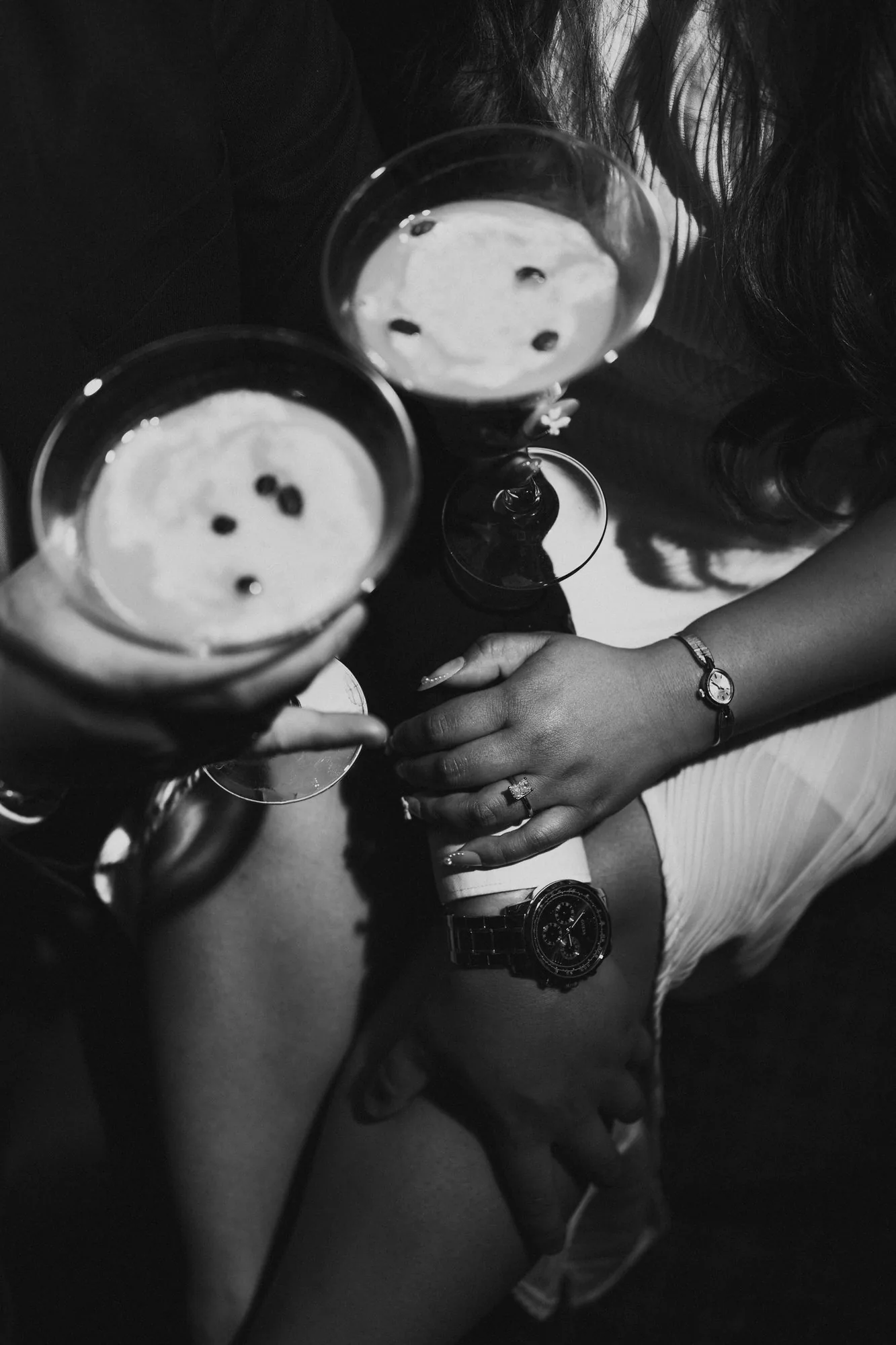 Black and white close-up of couple's intertwined hands with engagement ring beside espresso martini glasses — detail wedding photography by Ngo Photography Winnipeg